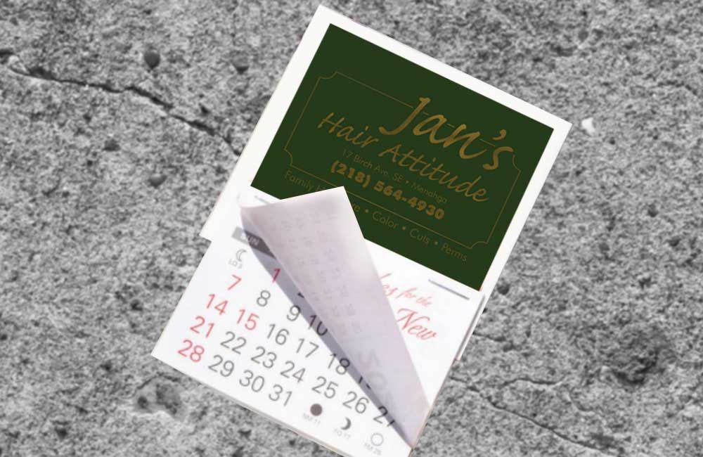 Calendar with Jan's Hair Altitude logo on cracked asphalt, page being turned.