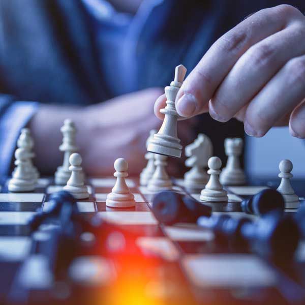 Hand moving white chess king on a board. Fallen black pieces scattered around.