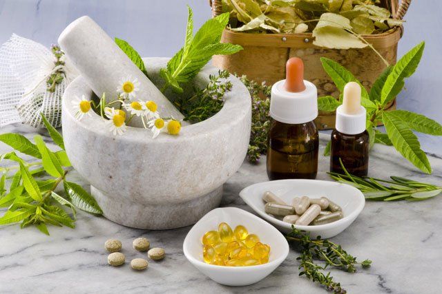 A mortar and pestle surrounded by herbs and pills on a table.