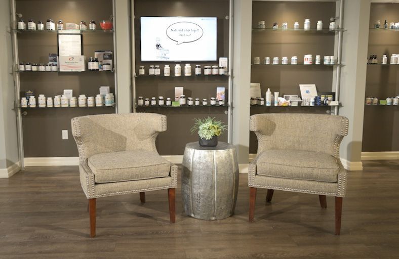 There are two chairs and a table in the room in front of a wall of supplements & other products.