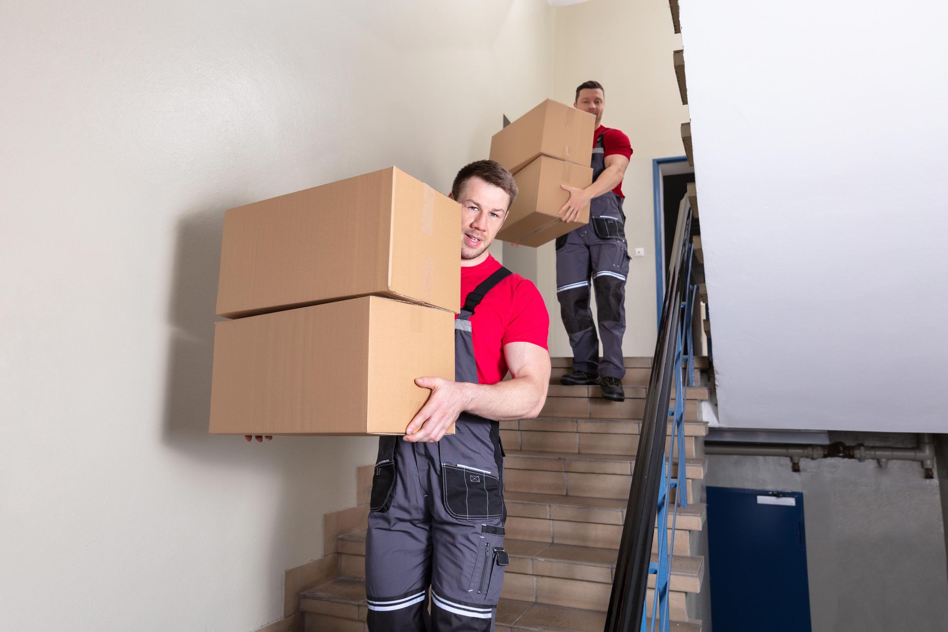 Professional movers carrying cardboard boxes down apartment stairs during moving service.