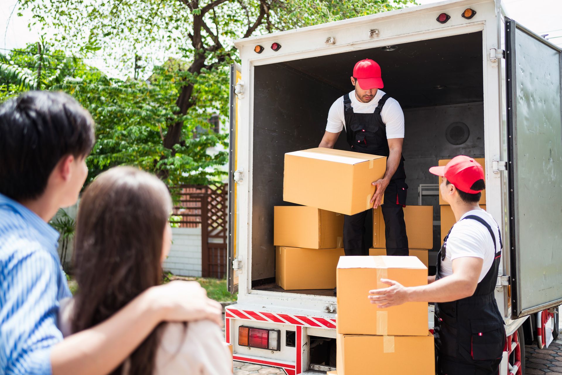 Young Couple watches two moving company’s workers loading a truck with their stuff. Young Couple watches two moving company’s workers loading a truck with their stuff.