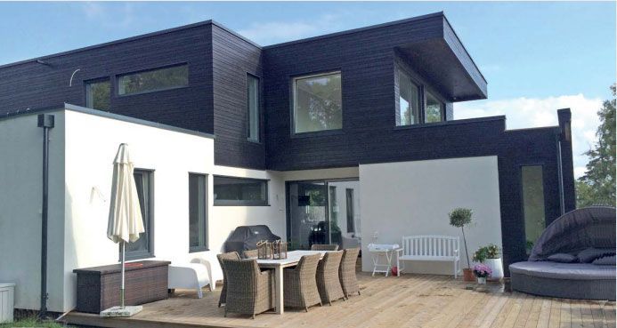 Moderne toetasjes hus med svart og hvitt eksteriør, treterrasse, utendørs spisegruppe og parasoll.