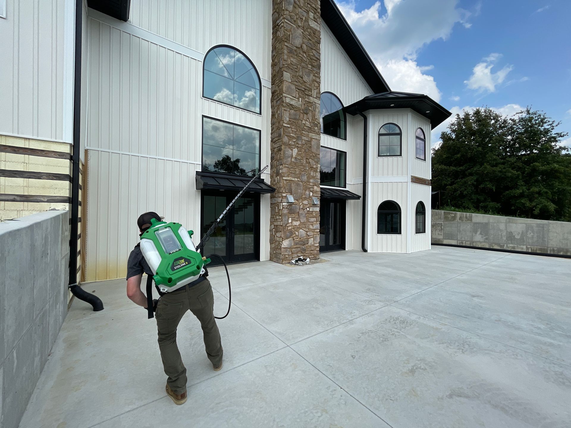 A man is spraying a building with a backpack sprayer.