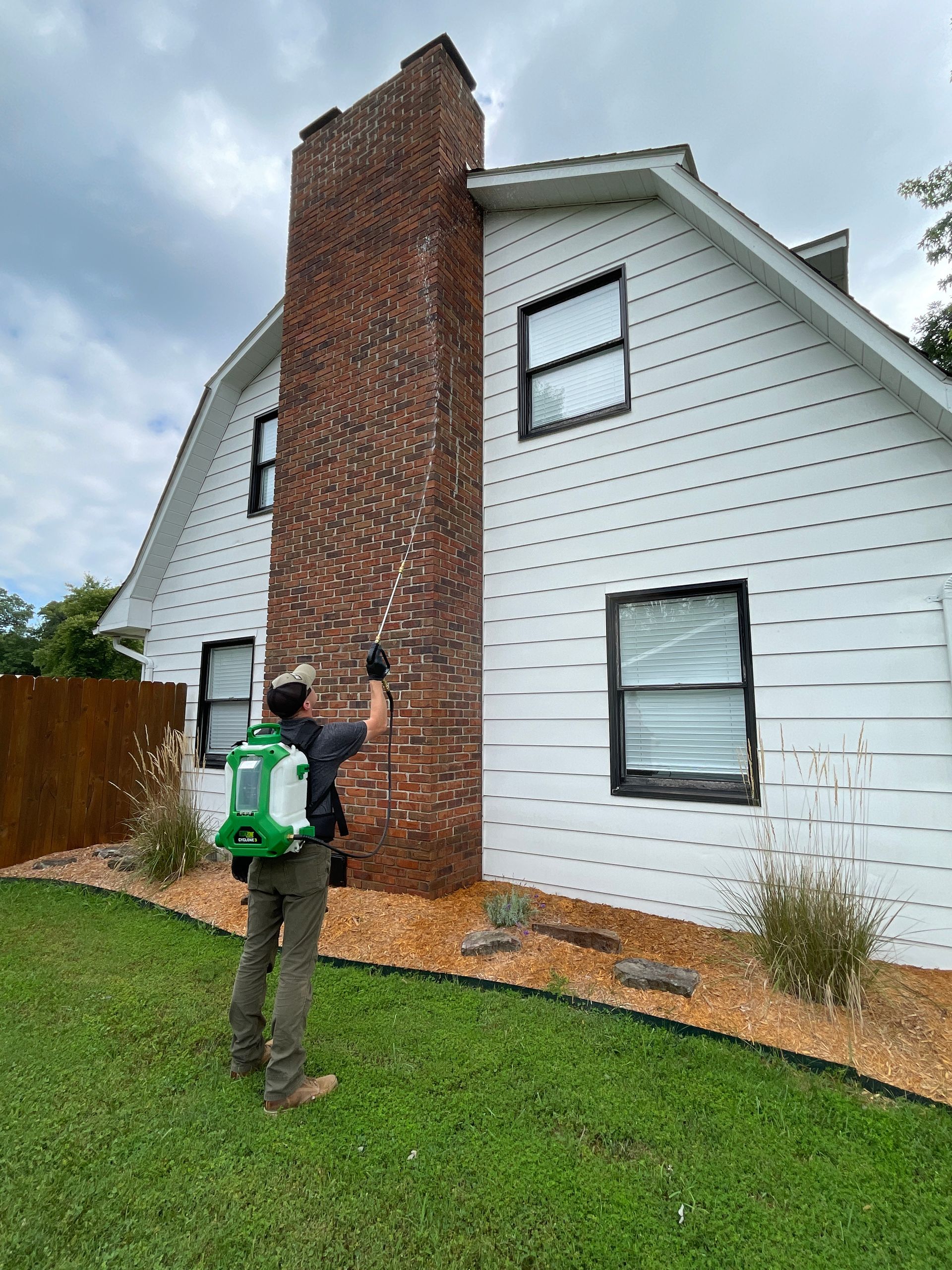 A man is standing in front of a white house with a brick chimney.