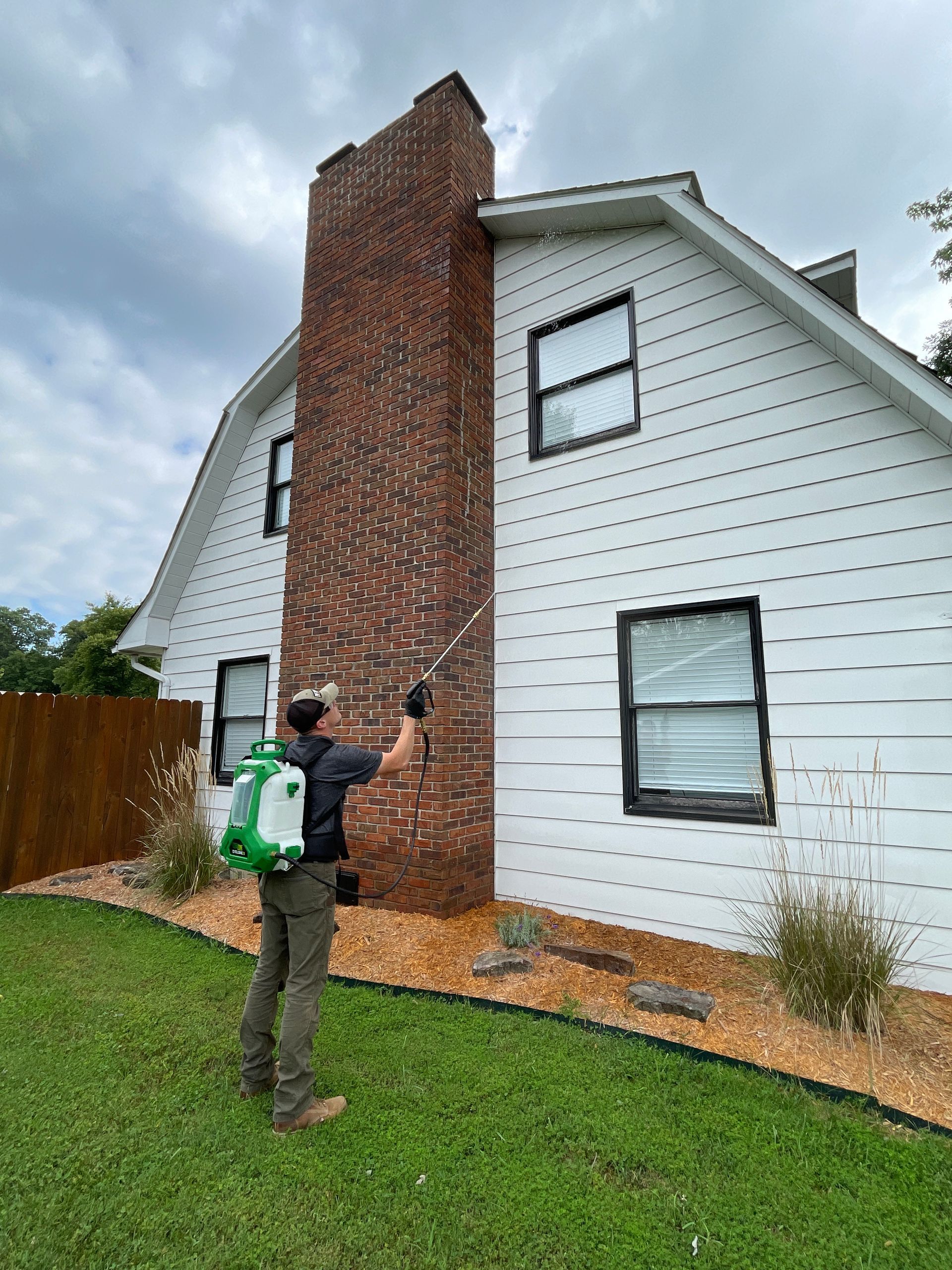 A man is spraying a brick chimney on a white house.