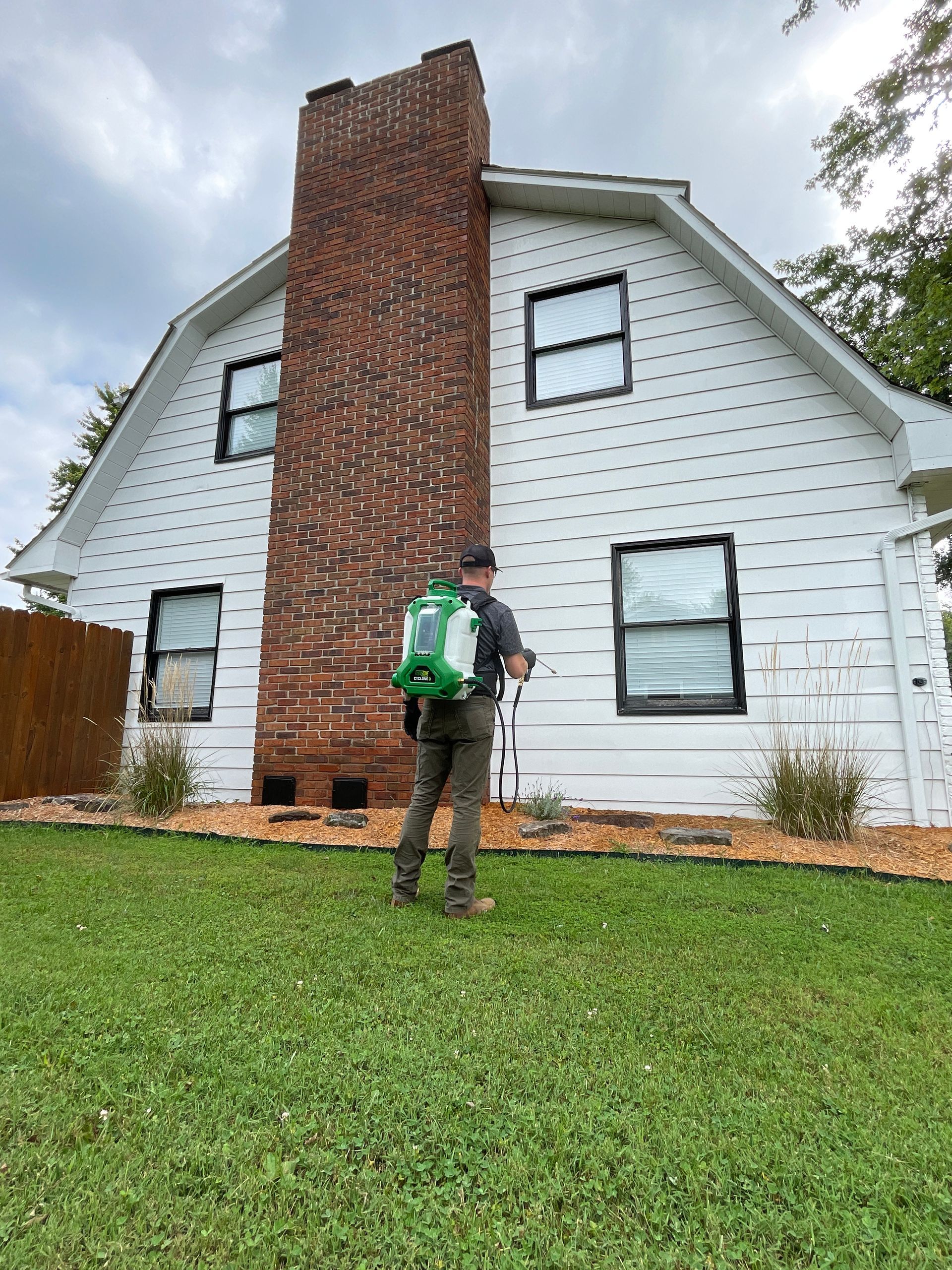 A man is spraying a lawn in front of a white house.
