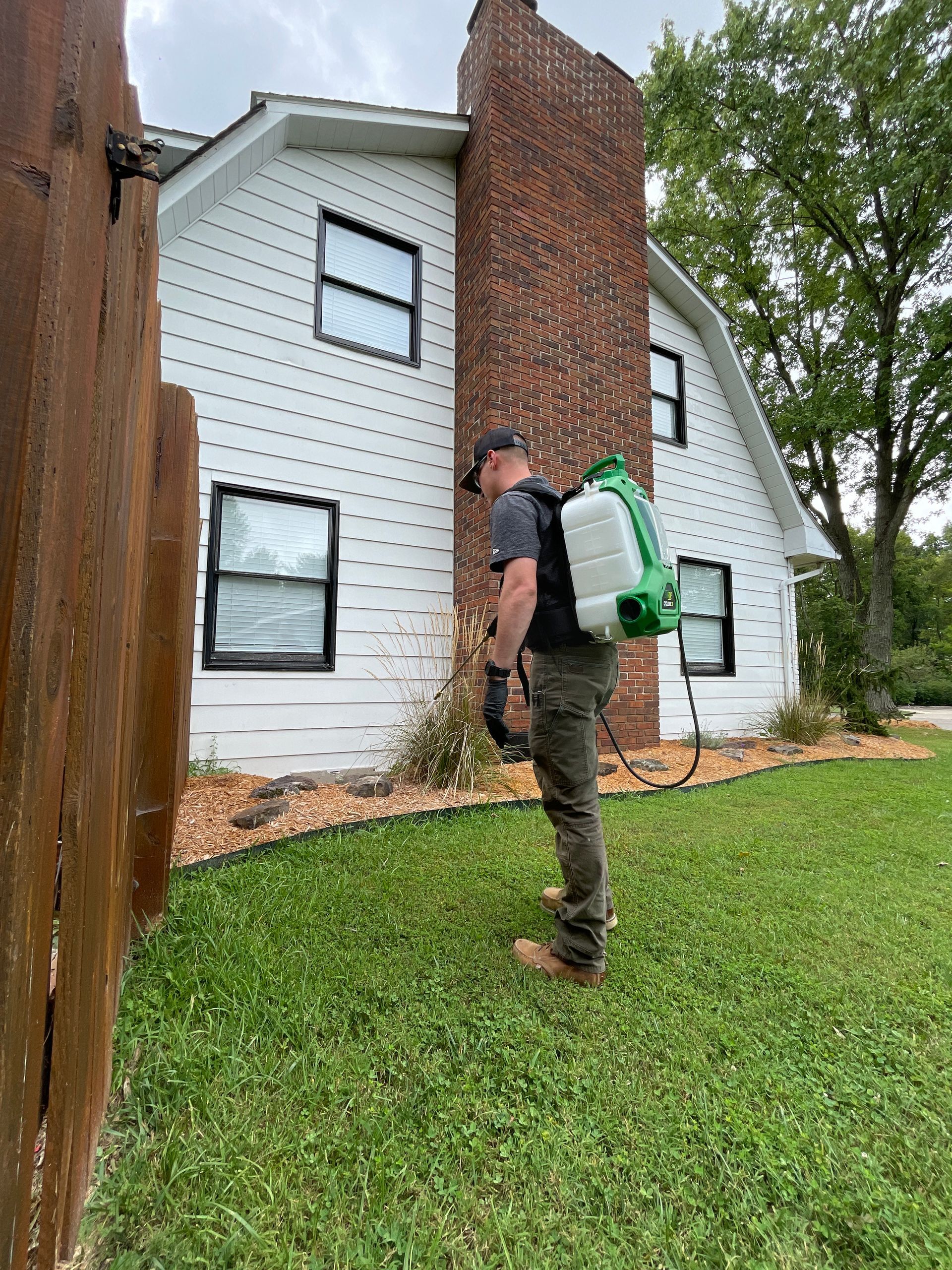 A man is spraying a lawn in front of a house.