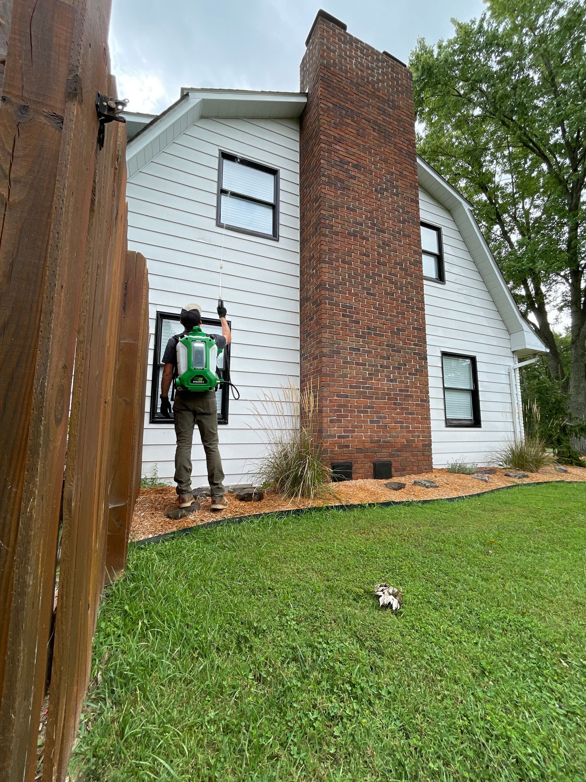 A man is standing in front of a white house with a brick chimney.