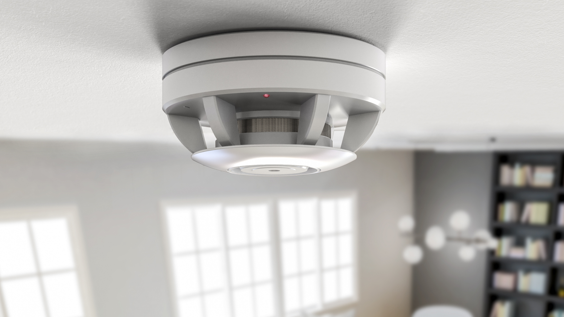White smoke detector mounted on a white ceiling in a room with a blurred background.