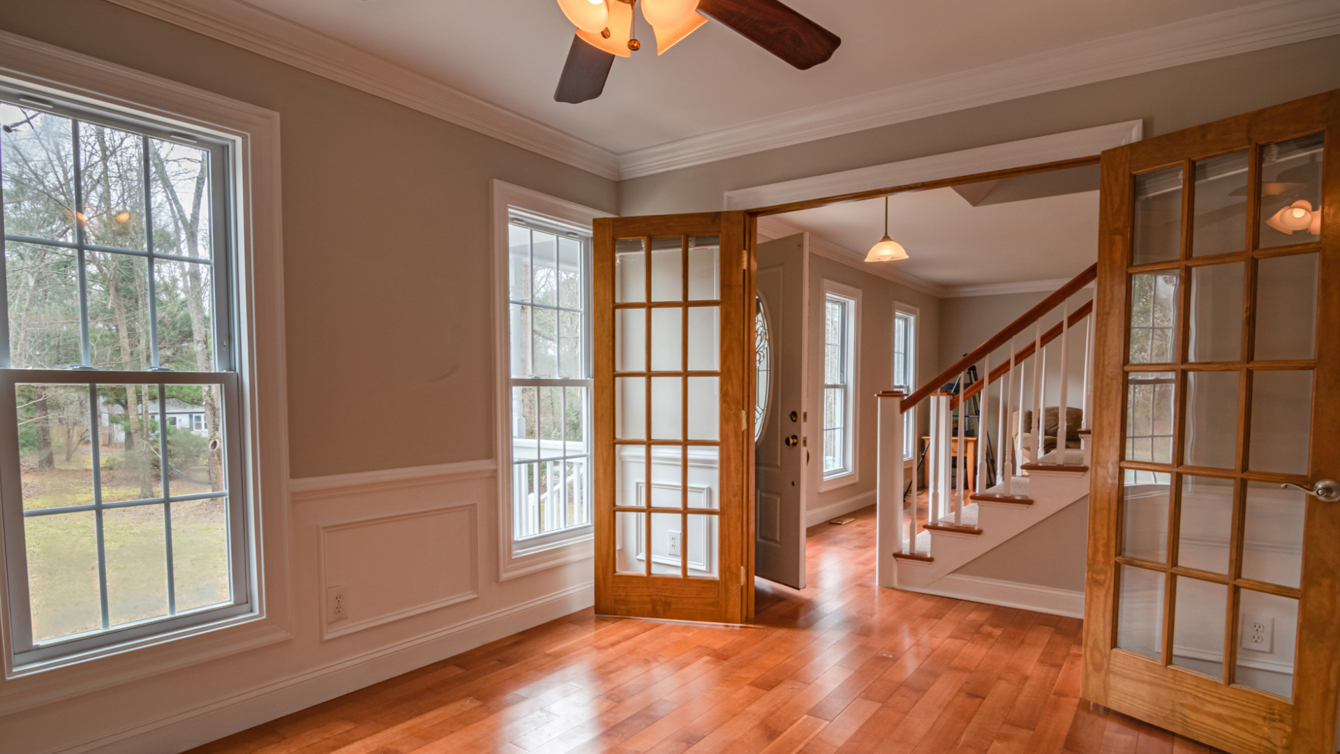 Empty room with wood floors, French doors, windows, and a staircase.