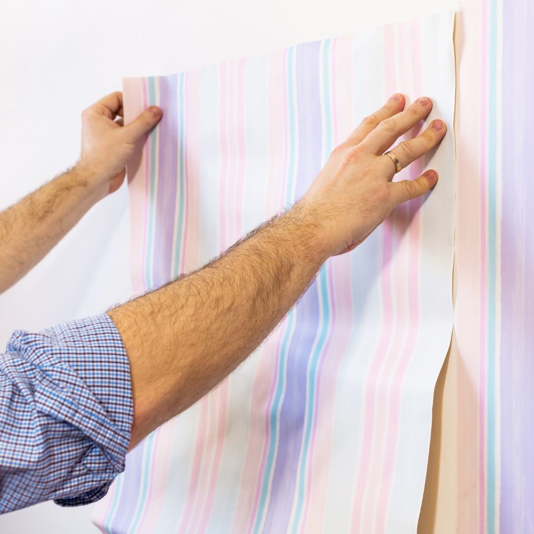 Person applying striped wallpaper to a wall, hands and arms visible.