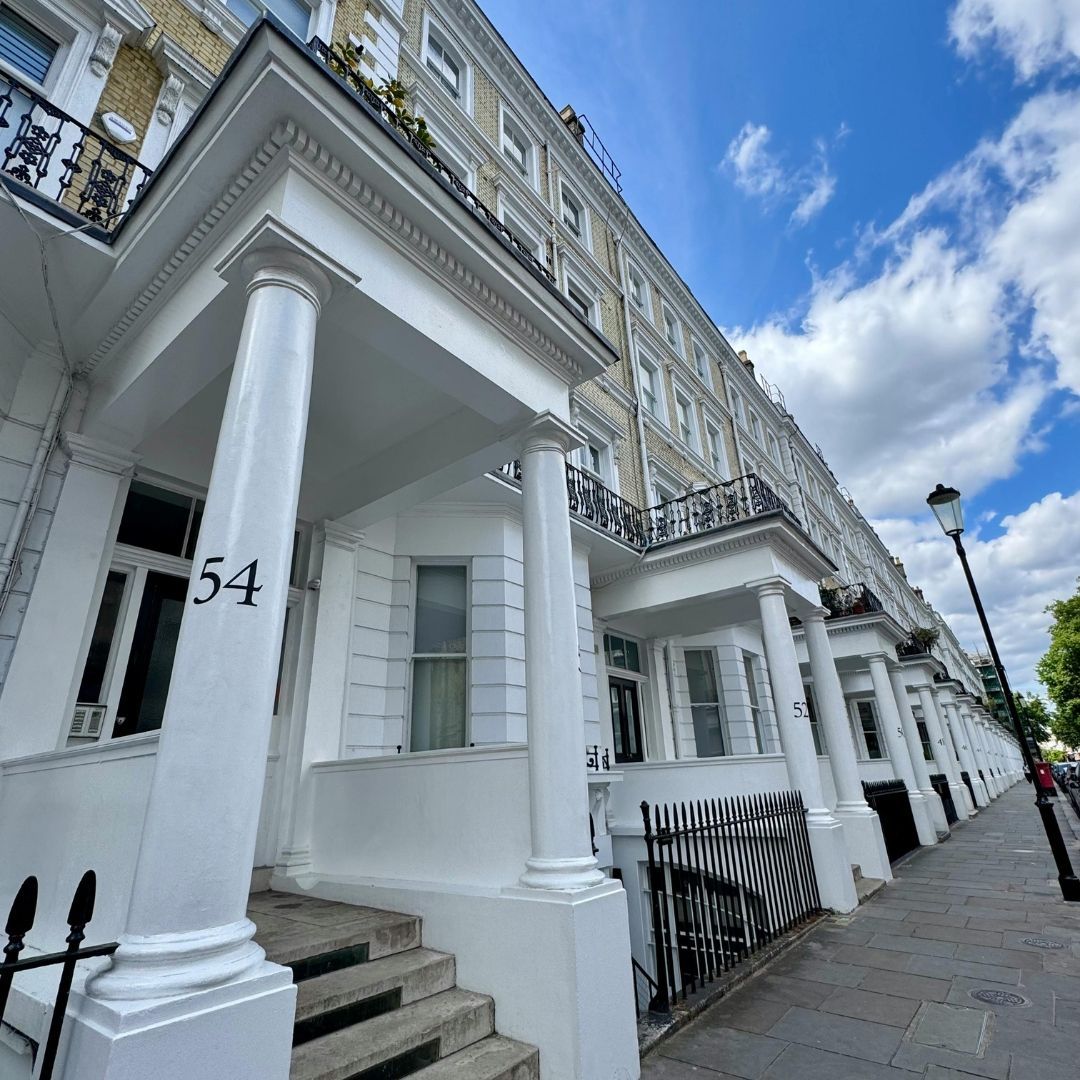 Row of white townhouses with columns and balconies under a blue sky. Number 54 is visible.