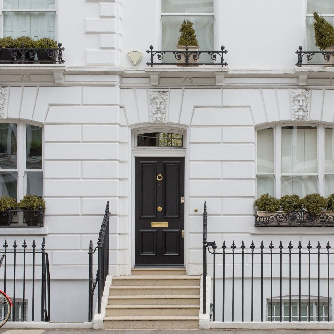White townhouse facade with black door, windows, and wrought-iron railings. Plant boxes and small topiary.
