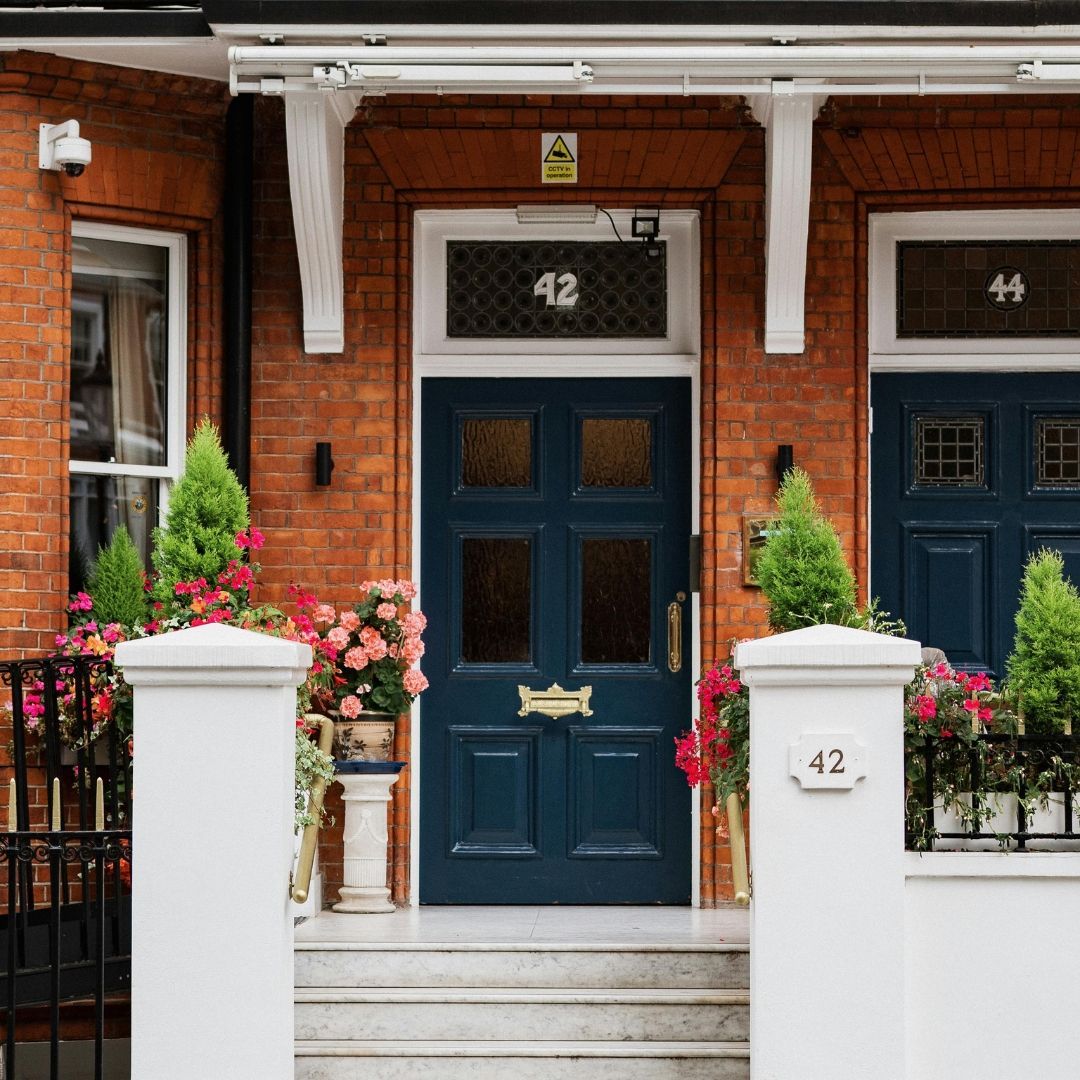 Blue door of house number 42 with brick facade and flowering plants.