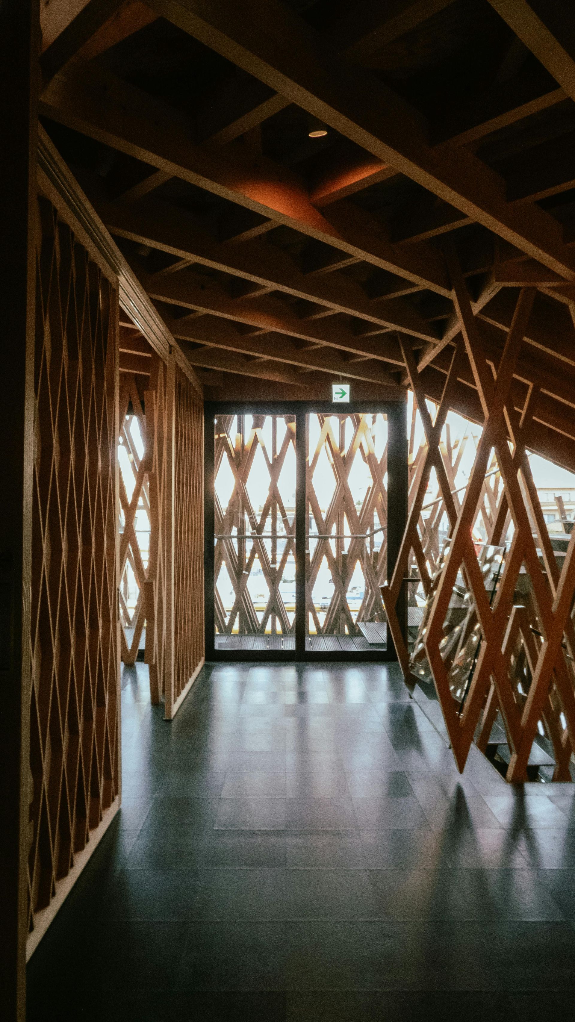 Wooden geometric interior with diamond-patterned screens and an exit sign visible. Dark floor, warm light.