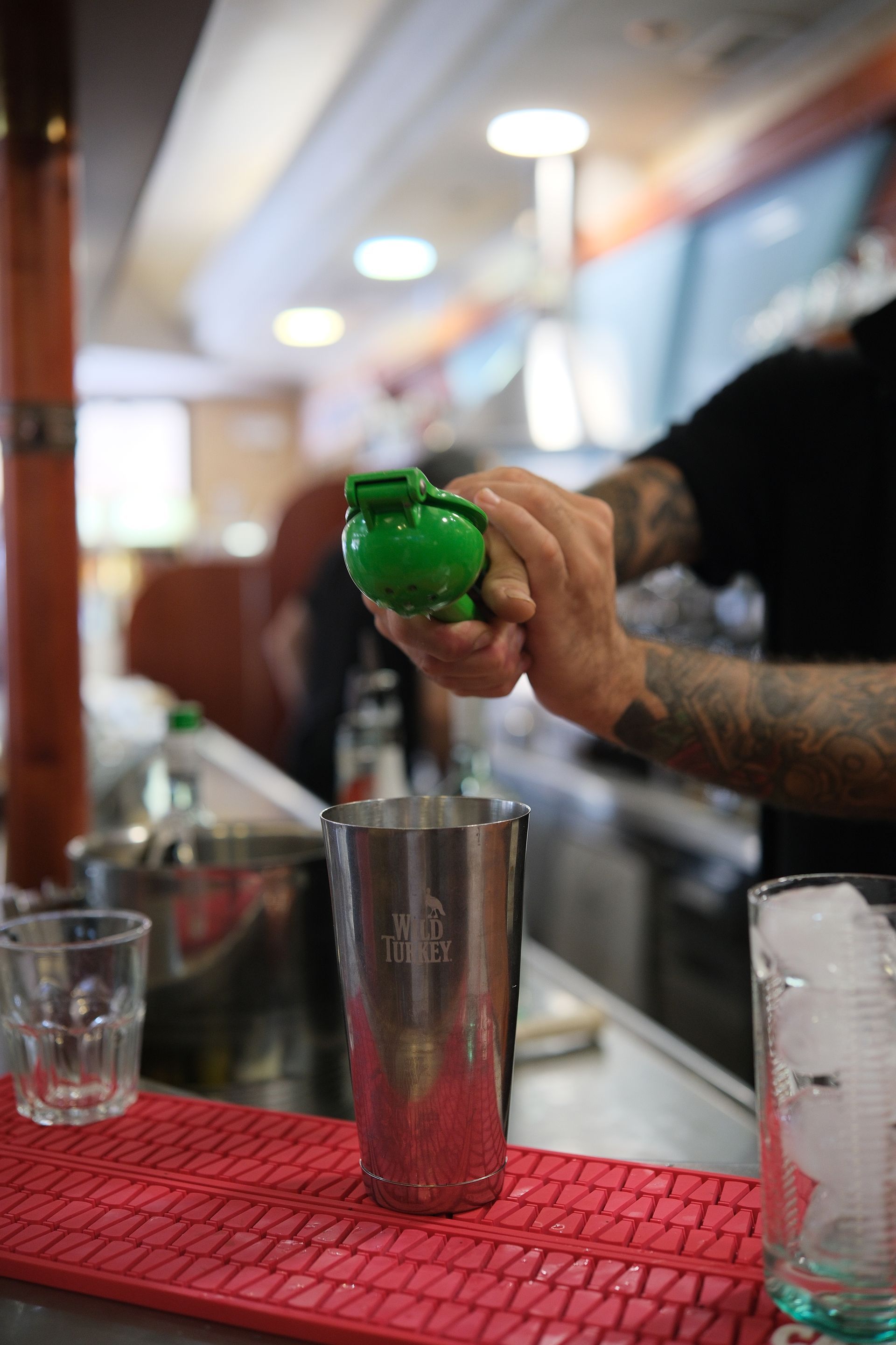 Barista che spreme il succo di lime in uno shaker. Tappetino rosso, shaker di metallo e bicchieri di ghiaccio.