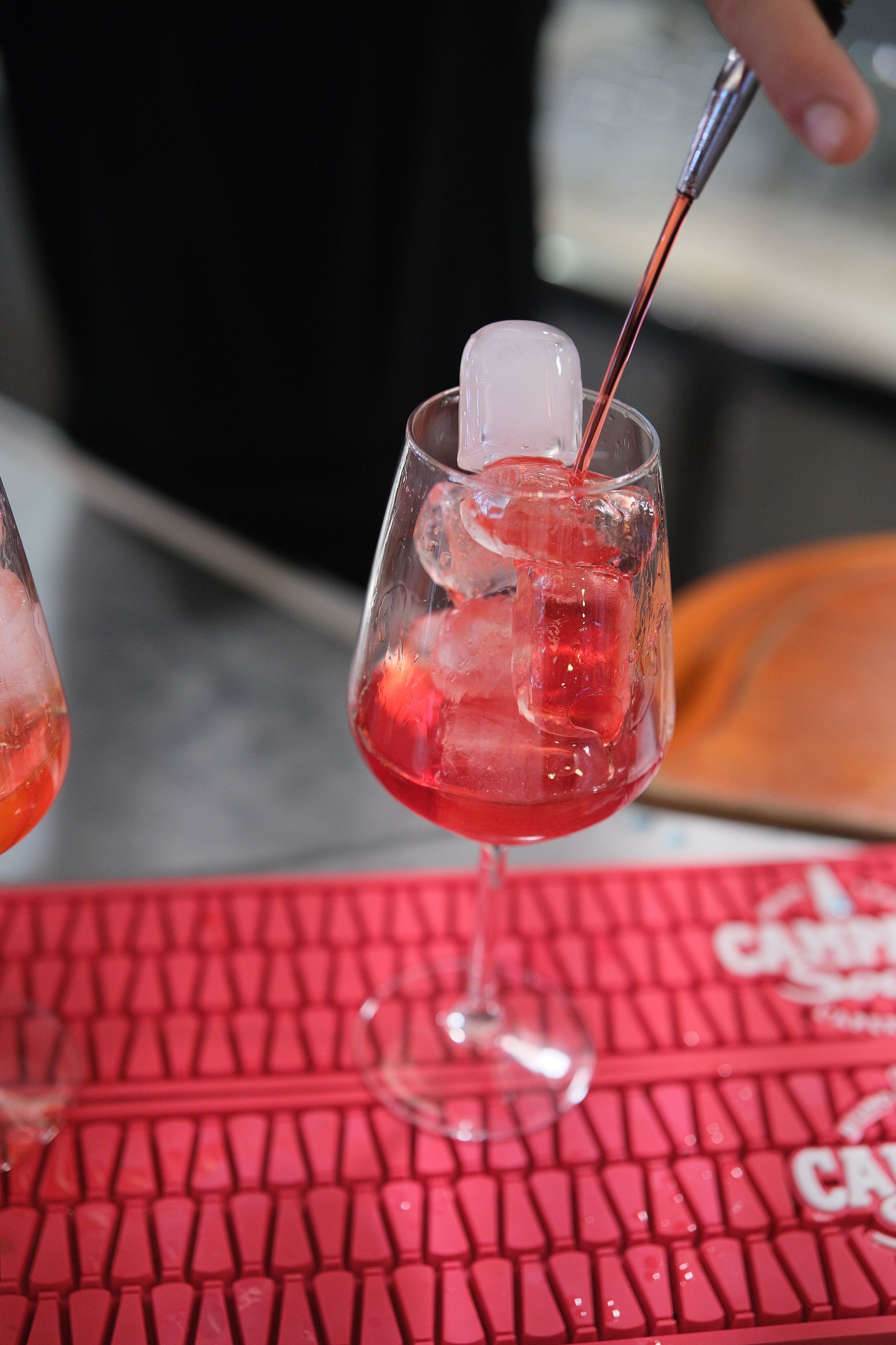 Cocktail rosso versato in un bicchiere con stelo e cubetti di ghiaccio. Ambiente da bar.