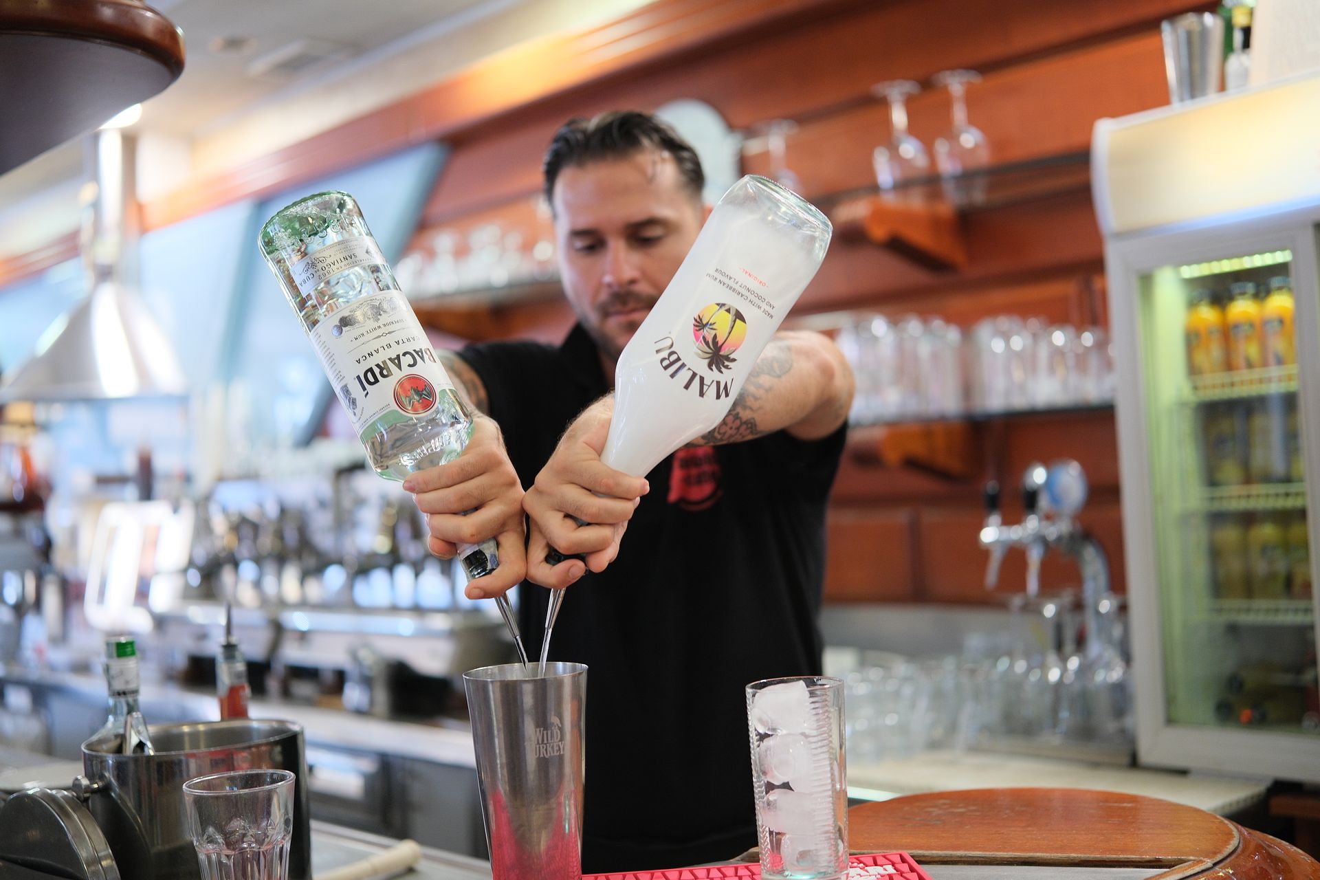 Barista che versa da due bottiglie in uno shaker al bar.