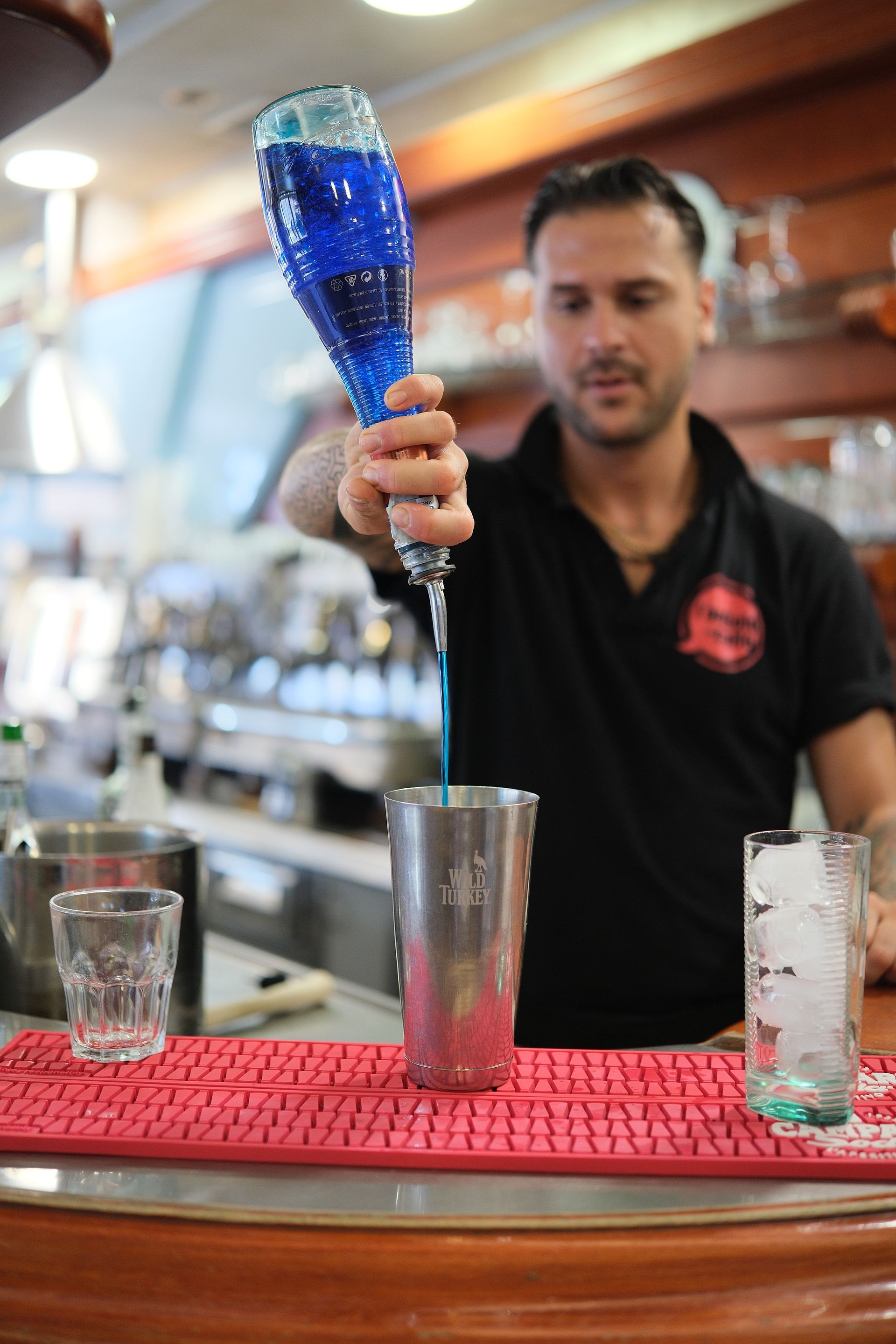 Barista che versa un liquido blu in uno shaker al bar.