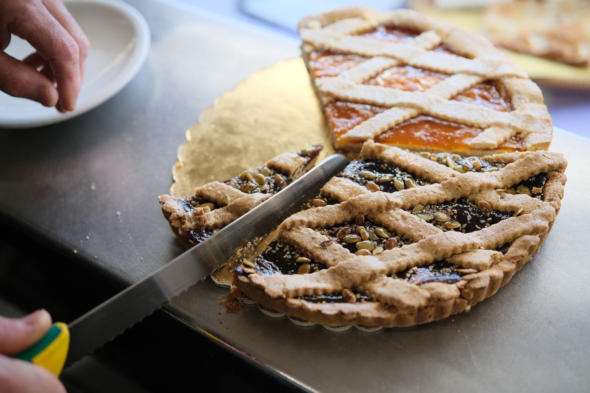 Una mano taglia una fetta da una crostata di frutta. 