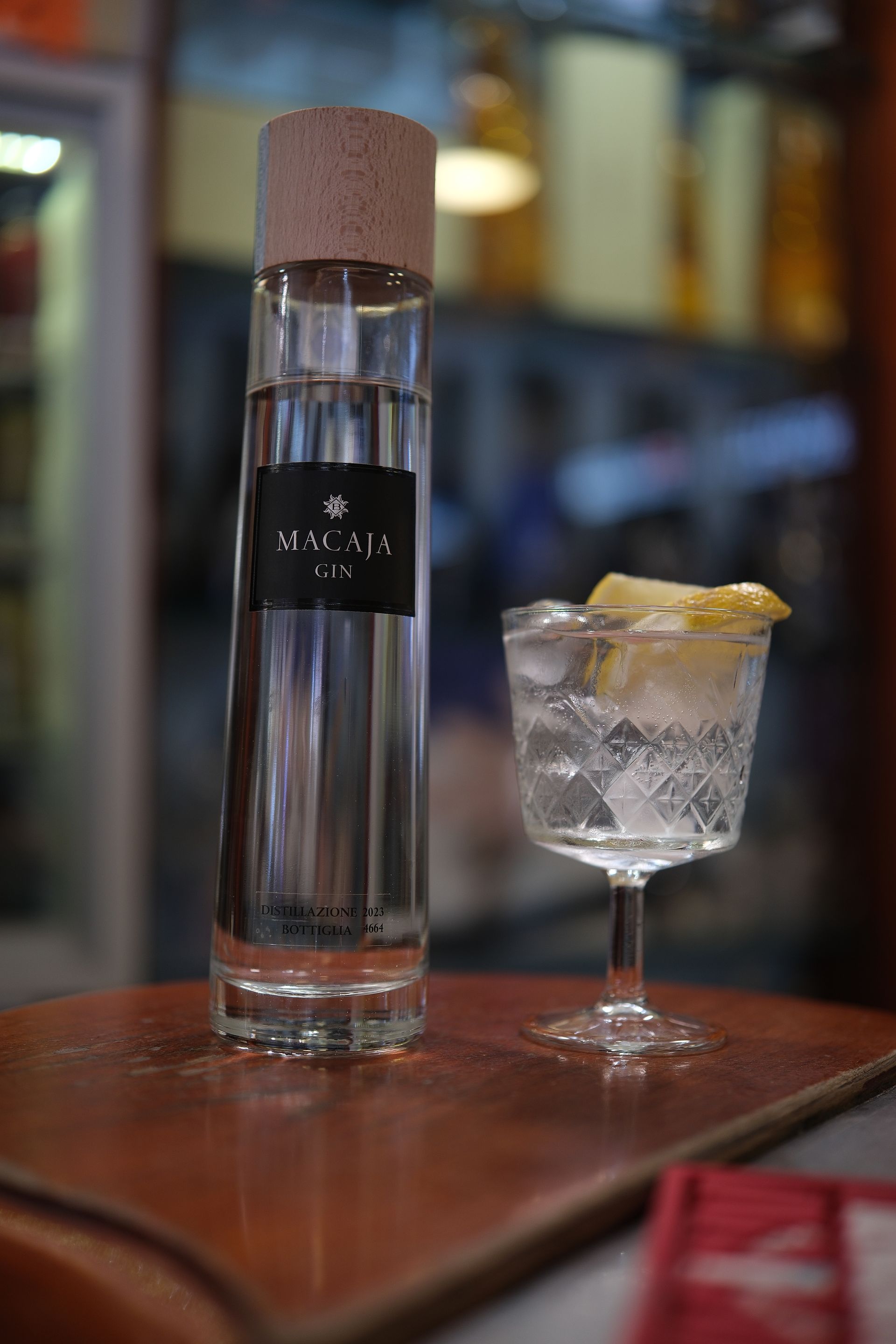 Bottiglia di gin e un cocktail in un bicchiere con ghiaccio e limone, su un tavolo.