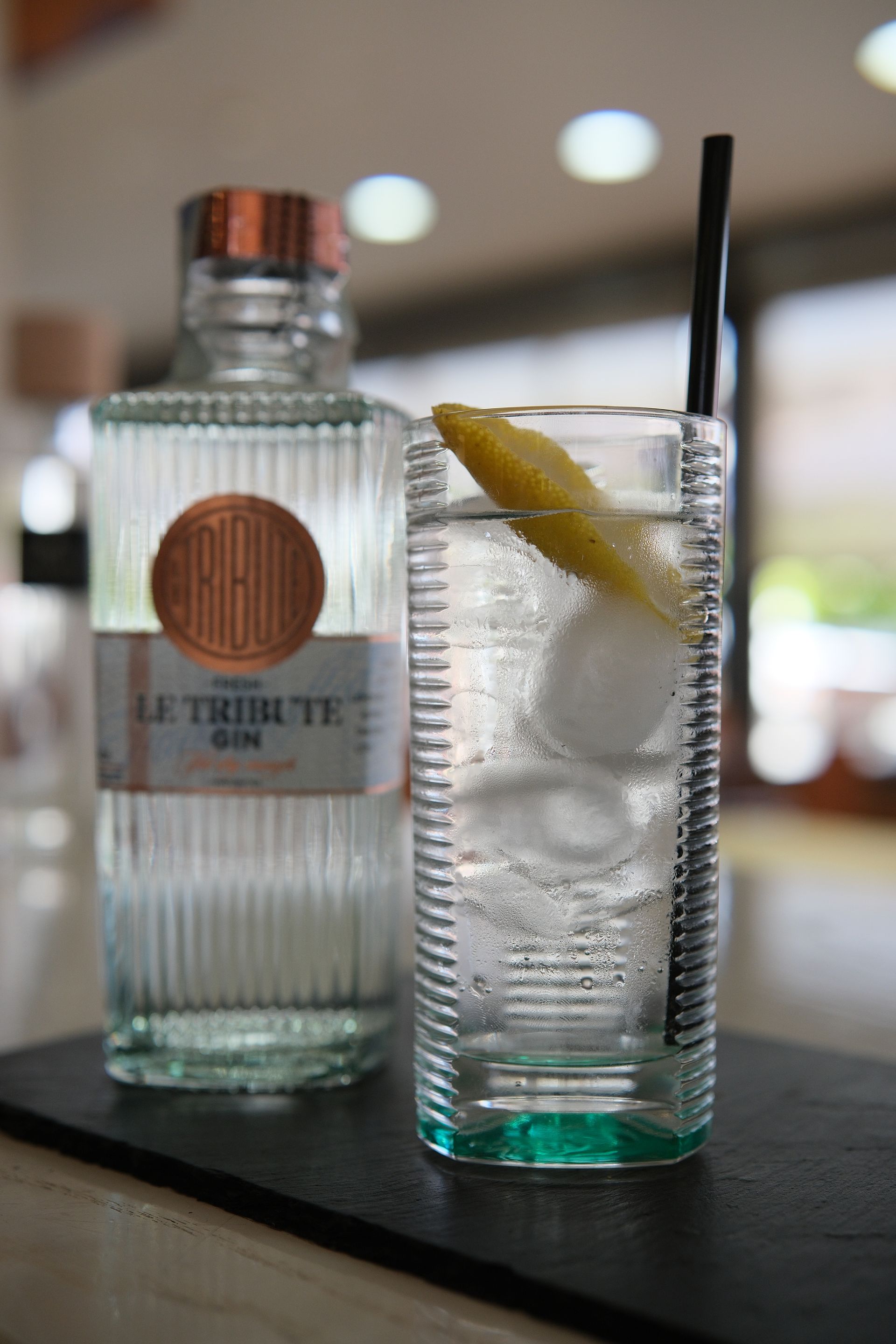 Cocktail al gin in un bicchiere alto con scorza di limone, accanto a una bottiglia di gin.