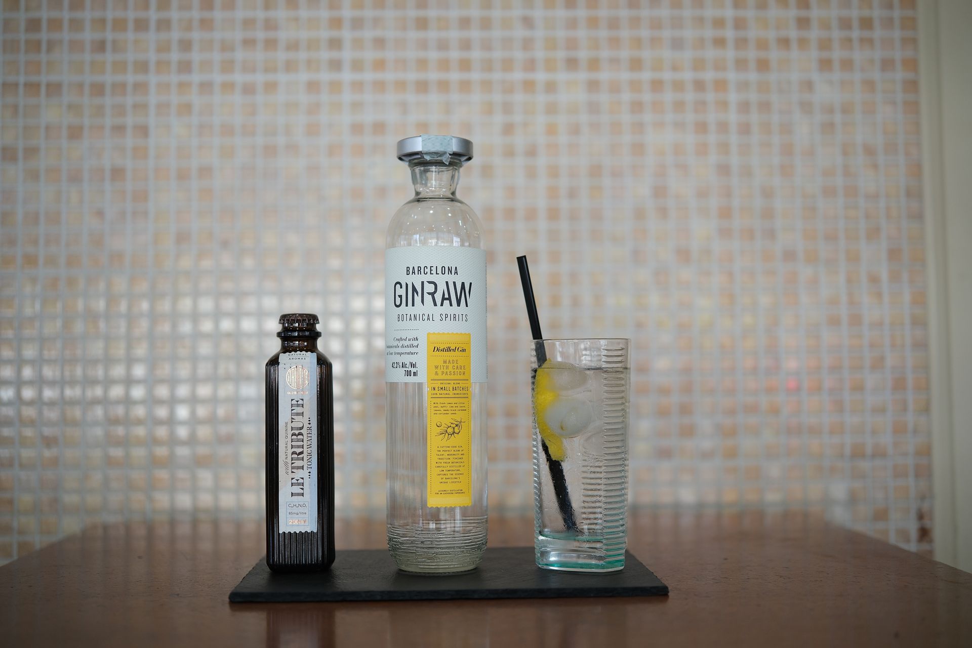 Bottiglie di liquore e mixer su un tavolo con un bicchiere di bevanda e una cannuccia nera.