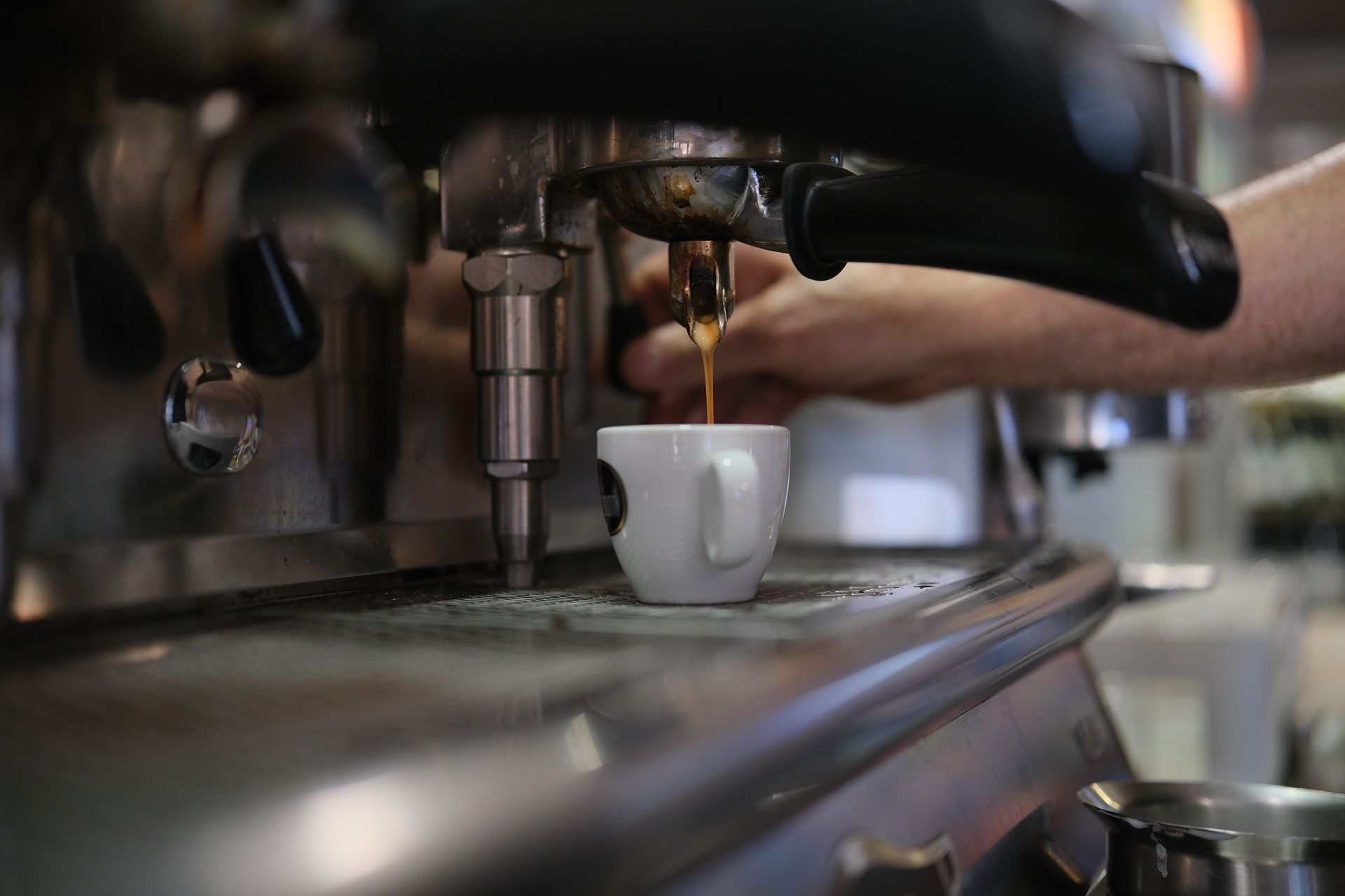 Macchina per caffè espresso che eroga il caffè in una tazza bianca; la mano del barista è lì vicino.