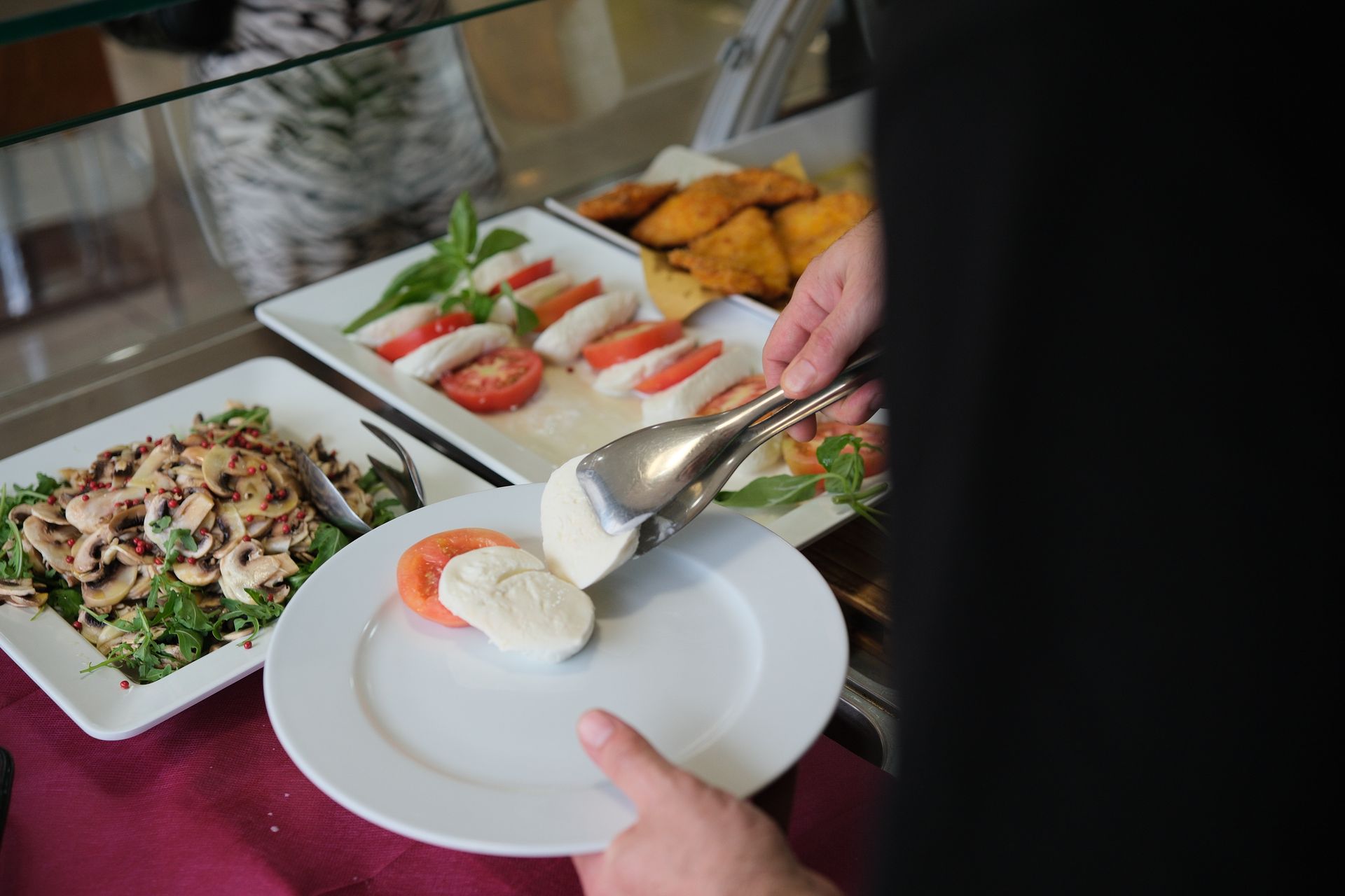Persona che usa le pinze per servire le fette di mozzarella e pomodoro su un piatto durante un buffet.