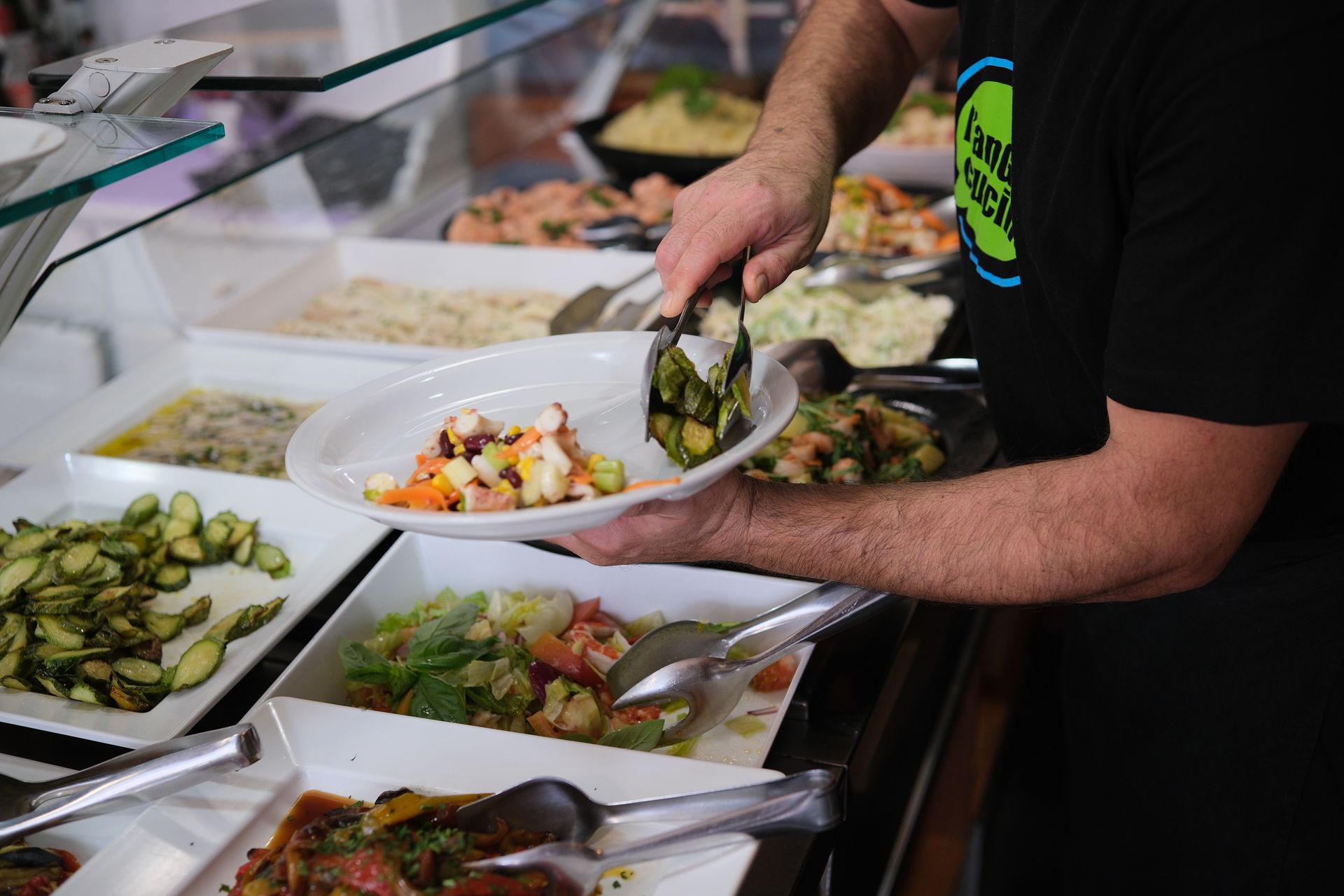 Uomo che usa le pinze per servire l'insalata da un buffet.