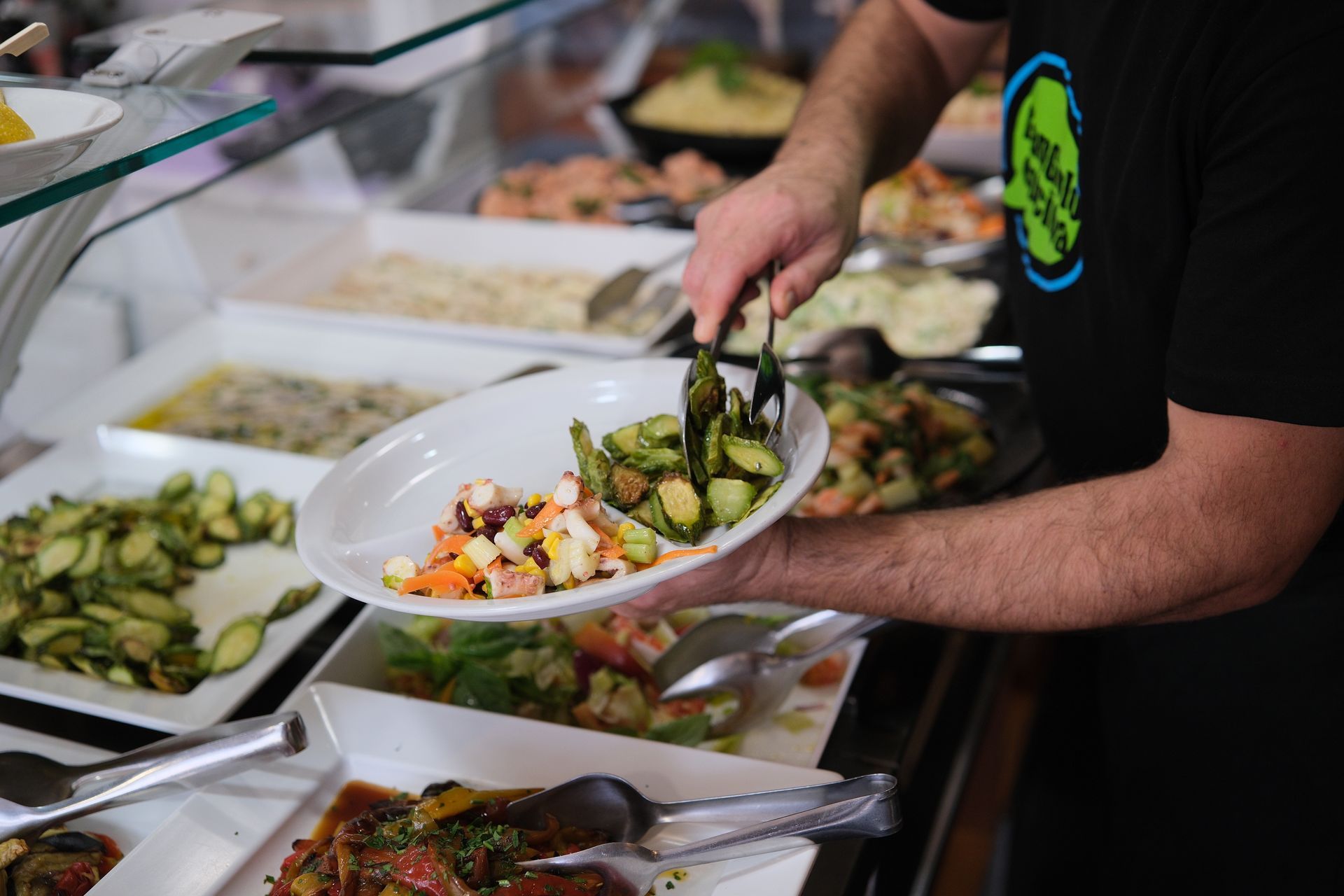Uomo che serve le verdure da un buffet, usando le pinze su un piatto bianco.