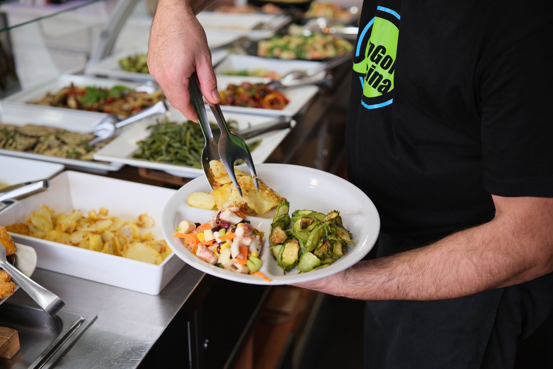 Una persona che serve cibo da un buffet, tenendo in mano un piatto con varie pietanze.