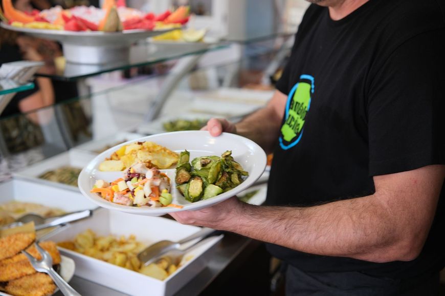 Uomo che tiene in mano un piatto di cibo a un buffet, sullo sfondo si vedono vari piatti.