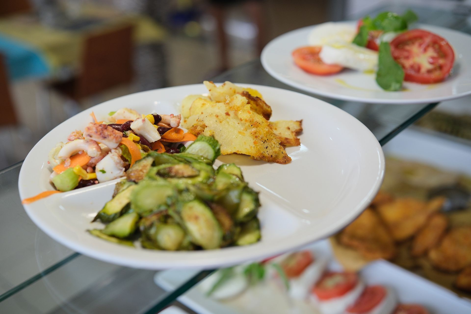 Piatti di cibo: insalata di polpo, patate arrosto, zucchine, insalata di pomodoro e mozzarella.