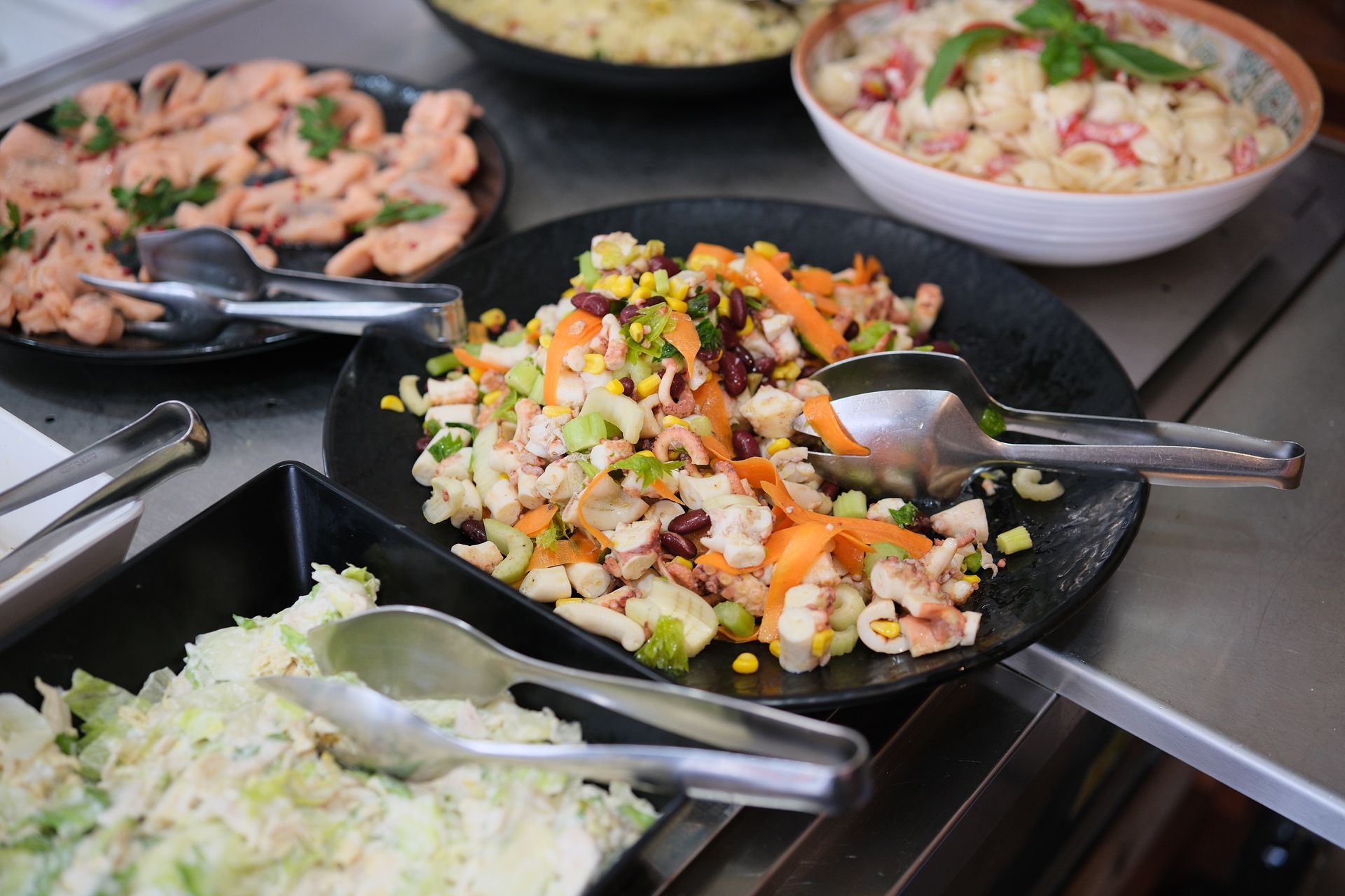 Buffet con varie insalate, tra cui pasta, salmone e insalata di cavolo.