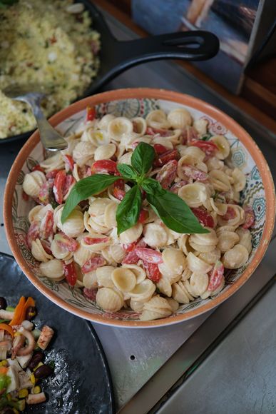 Una persona serve l'insalata di pasta da una vetrina insieme ad altri cibi preparati.