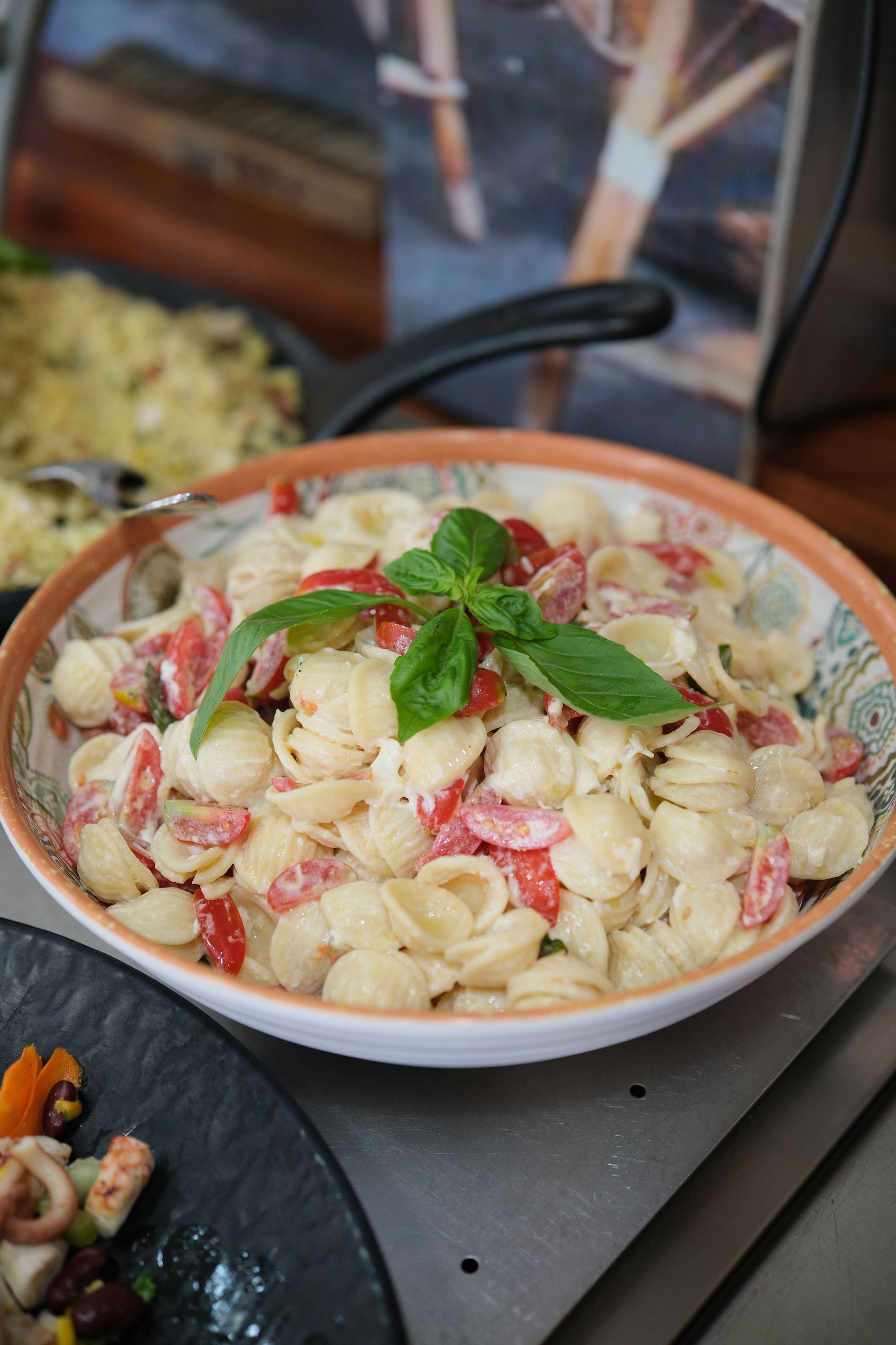 Insalata di pasta con pomodori e basilico in una ciotola decorativa.
