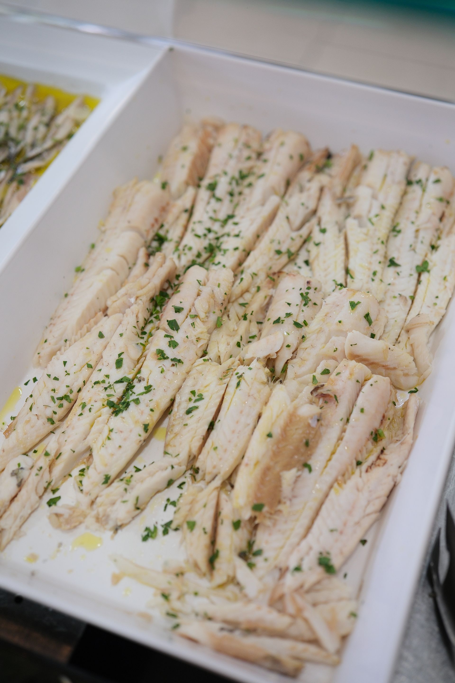 Vassoio rettangolare bianco con filetti di pesce affettati e cosparsi di erbe verdi.