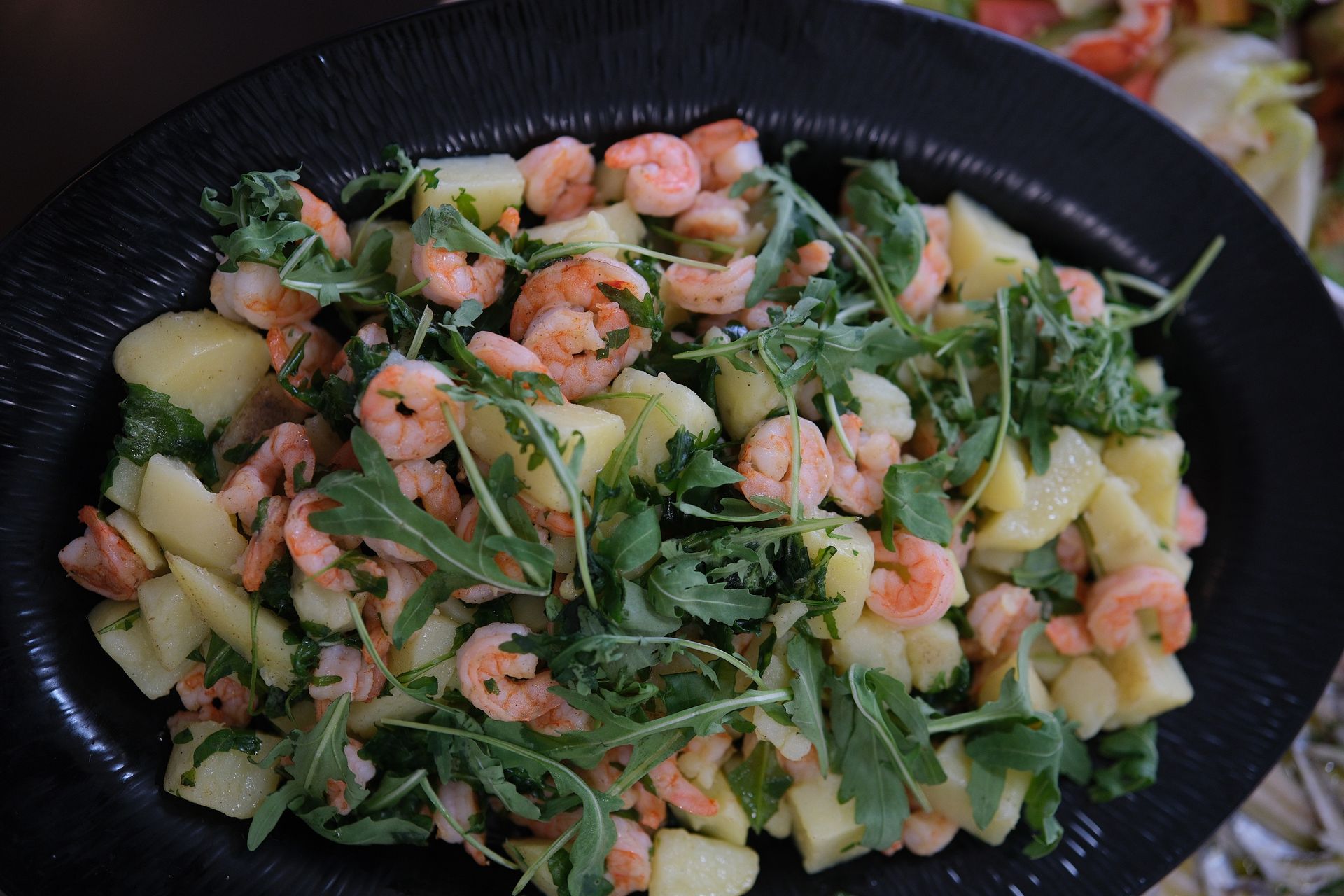 Insalata di gamberi con patate e rucola su un piatto nero.