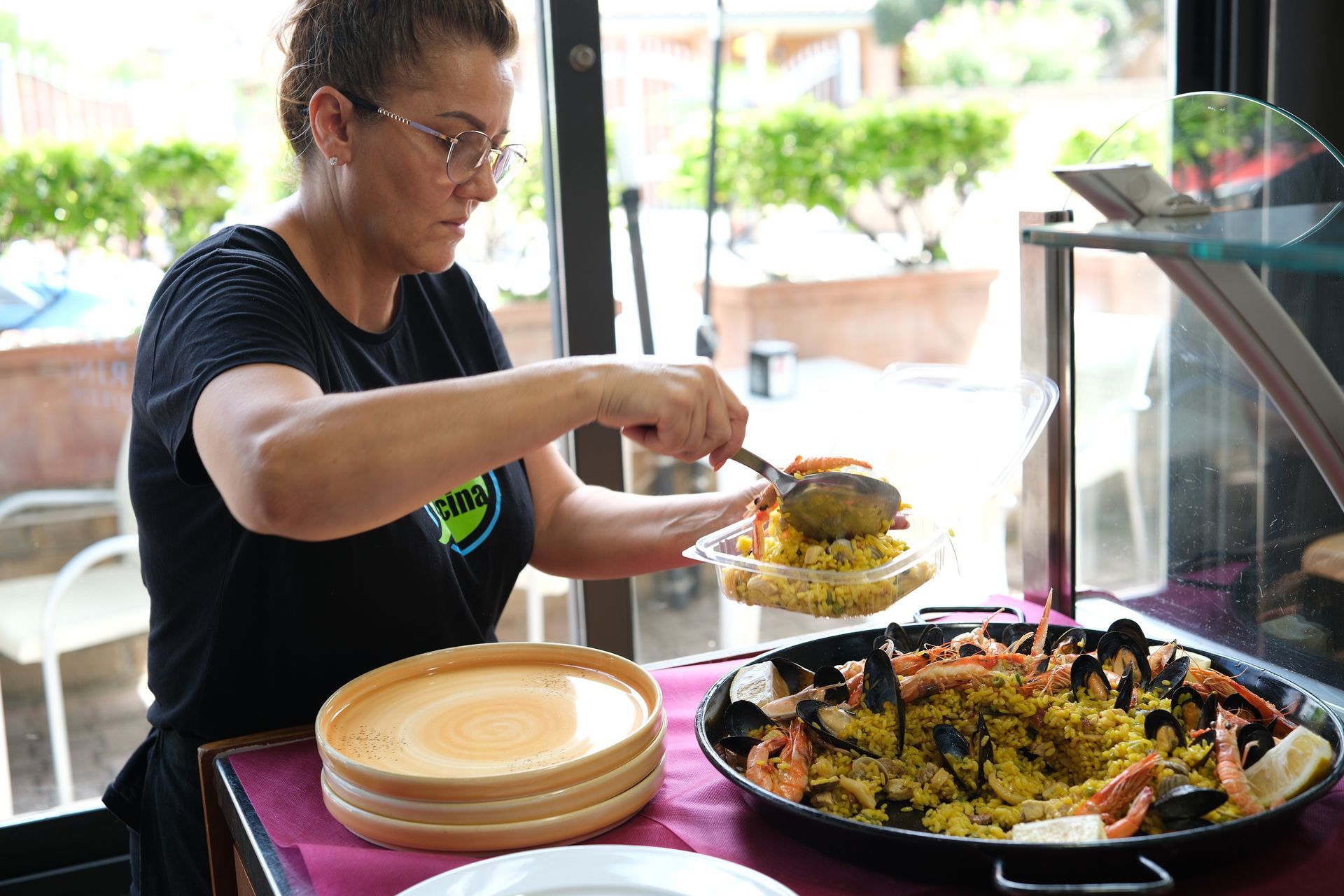Donna che serve la paella da una grande padella in un ristorante.