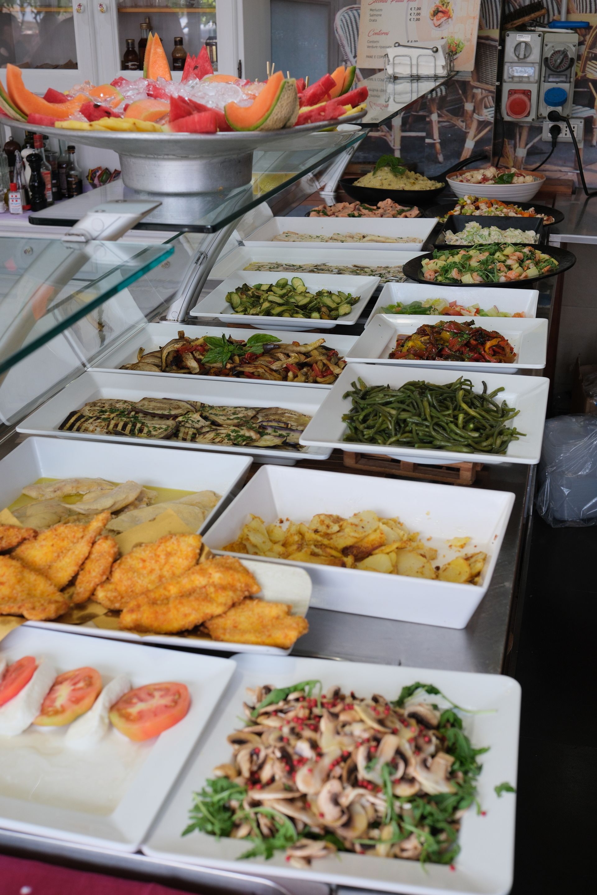 Esposizione a buffet di insalate, verdure e frutta di vario tipo in un ambiente luminoso da ristorante.