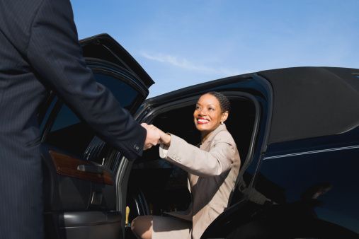 a woman is getting out of a limousine and shaking hands with a man .