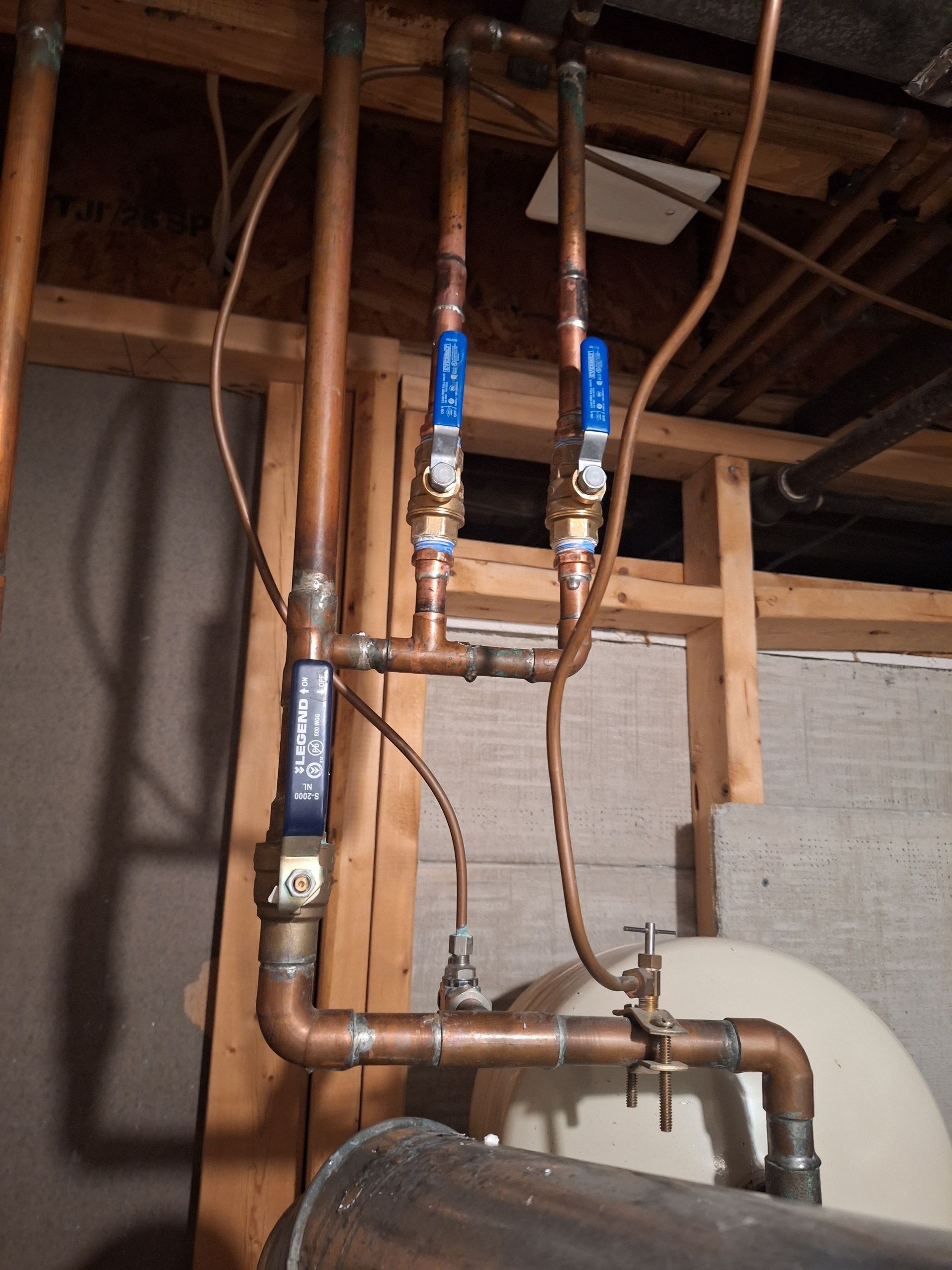 A copper pipe assembly with a valve and white-insulated piping mounted on a wooden post against a white wall.