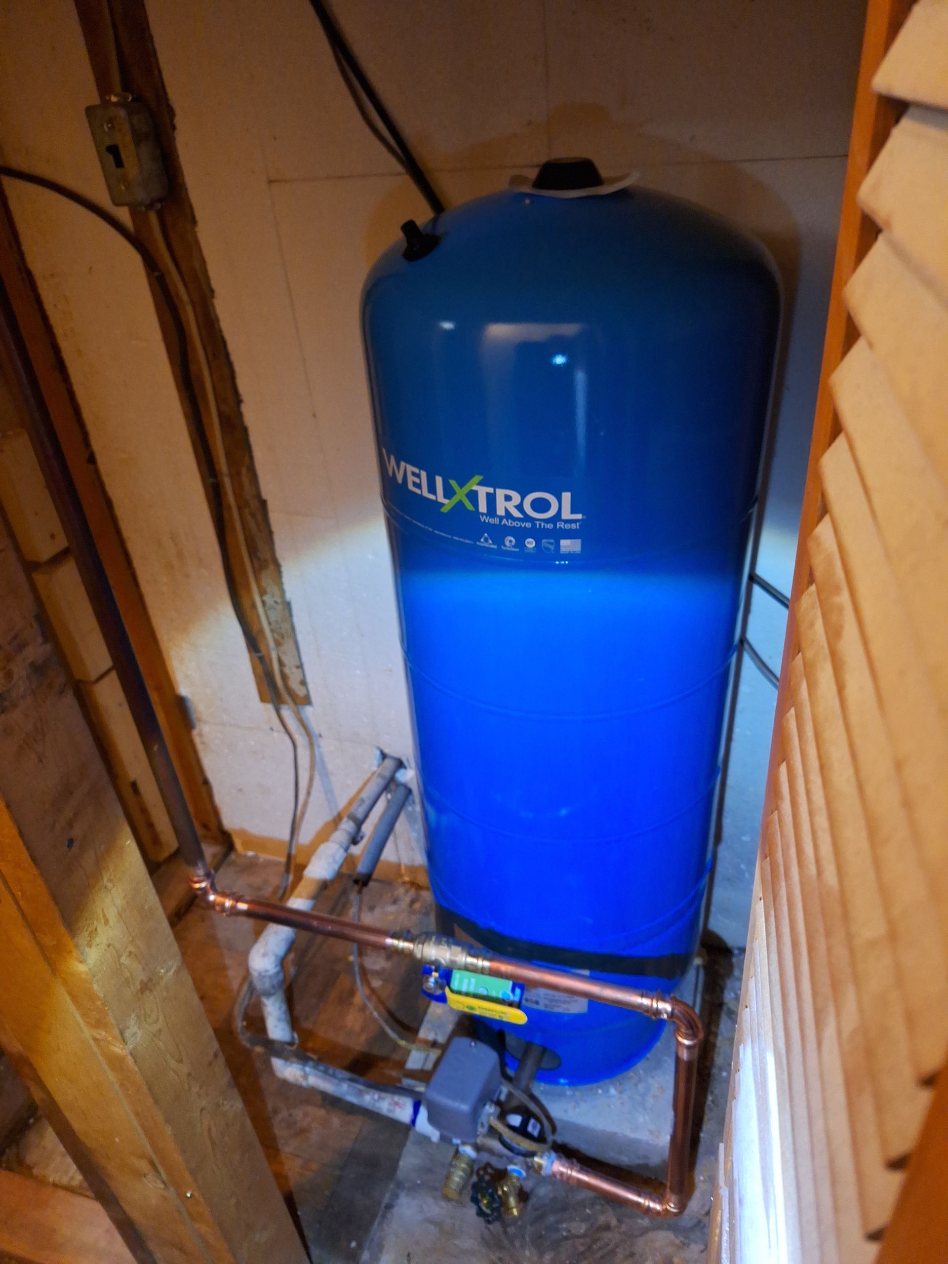 A Well-X-Trol blue water pressure tank connected to copper plumbing in a basement utility area.