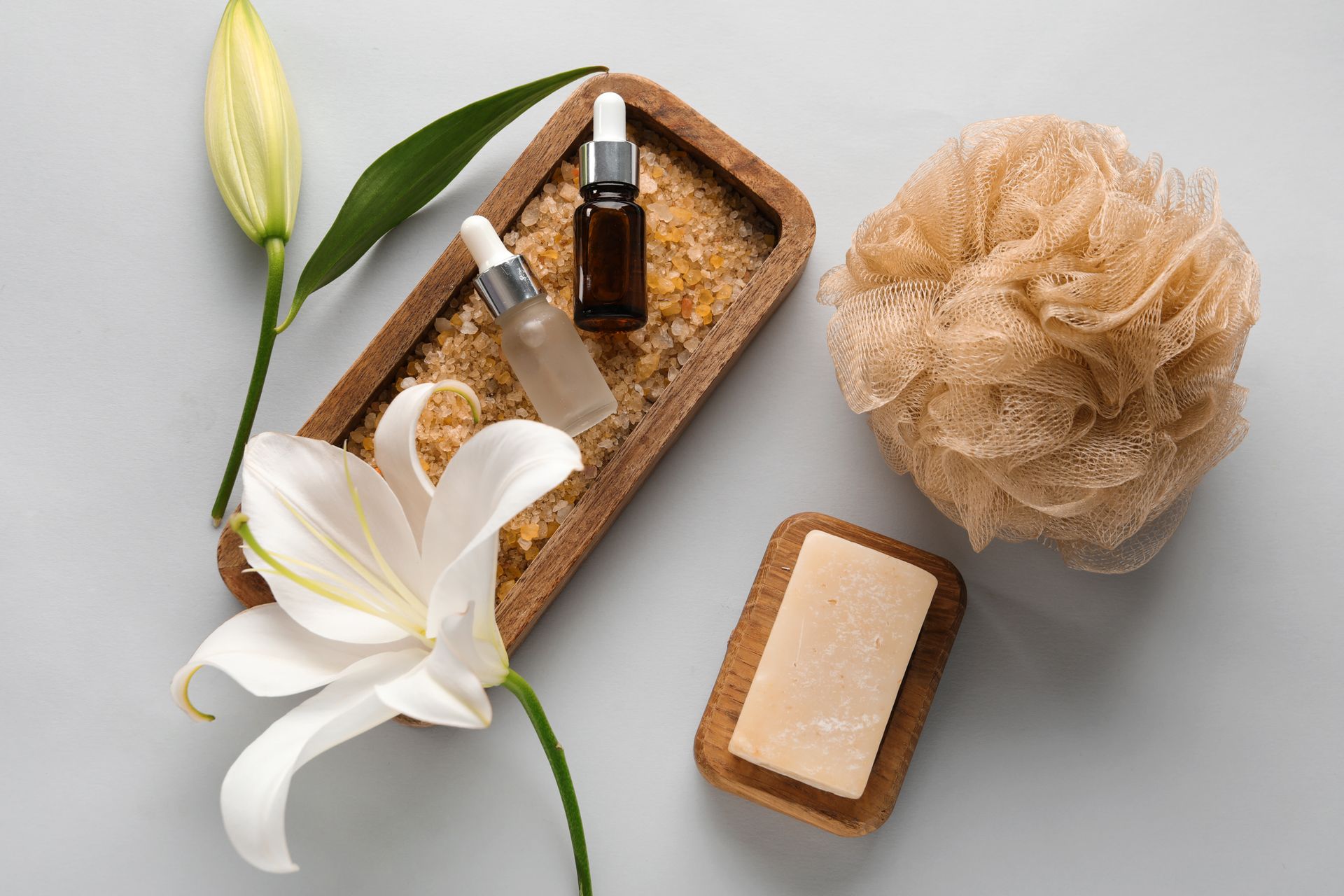 A wooden tray filled with soap , bottles , a flower and a sponge.