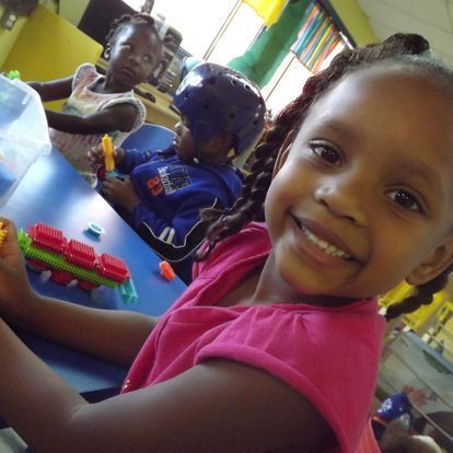 A little girl in a pink shirt is smiling at the camera