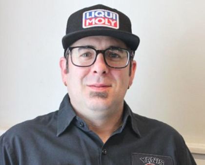 A man wearing a liqui moly hat and glasses is standing in front of a white wall.
