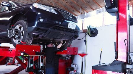 A man is working on a car on a lift in a garage.