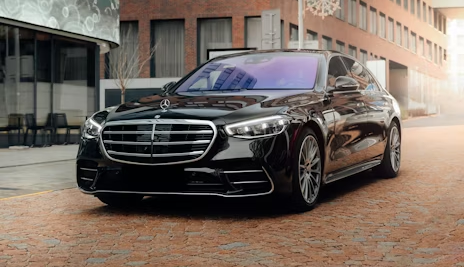 Black luxury sedan parked on a brick street between modern buildings under an overhang